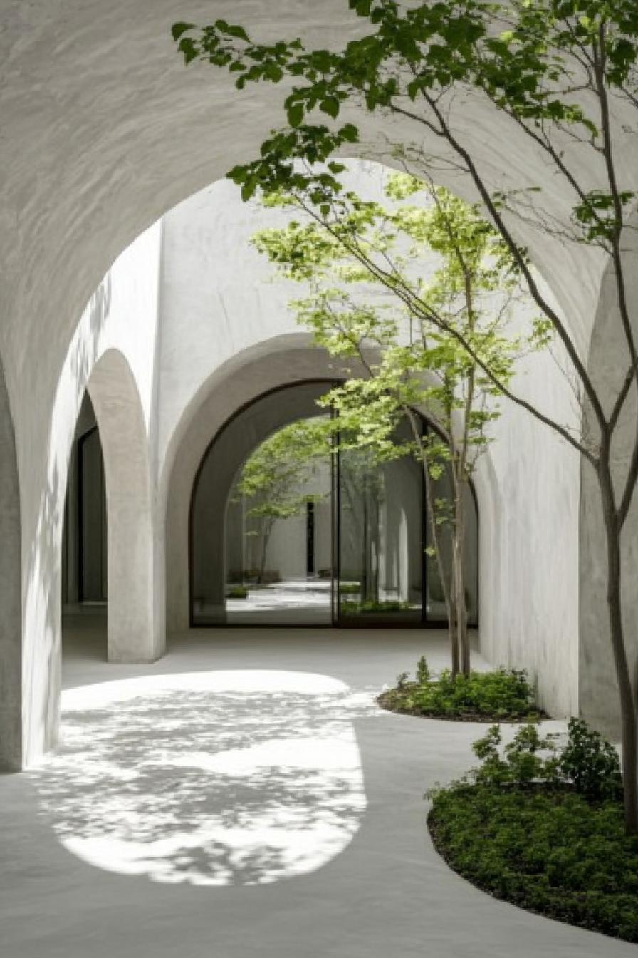 minimalist refined aesthetic courtyard architecture white concrete arches curved ceiling openings arched glass doors visible at far end concrete