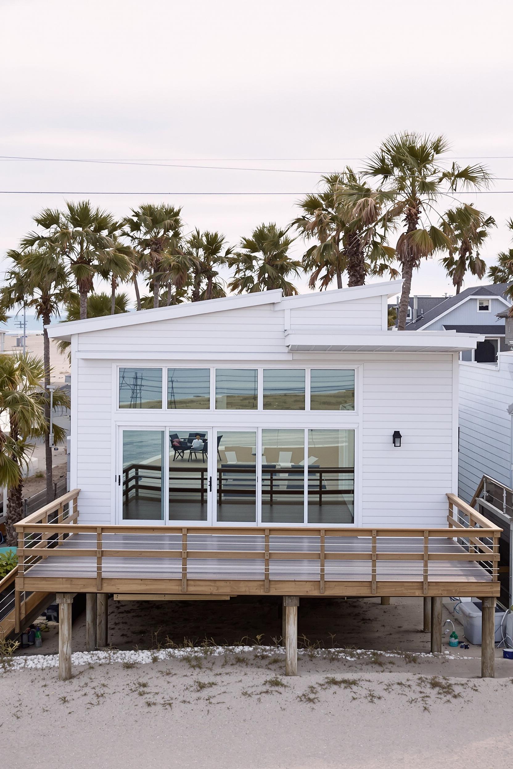 Small white beach house with large windows and a wooden deck