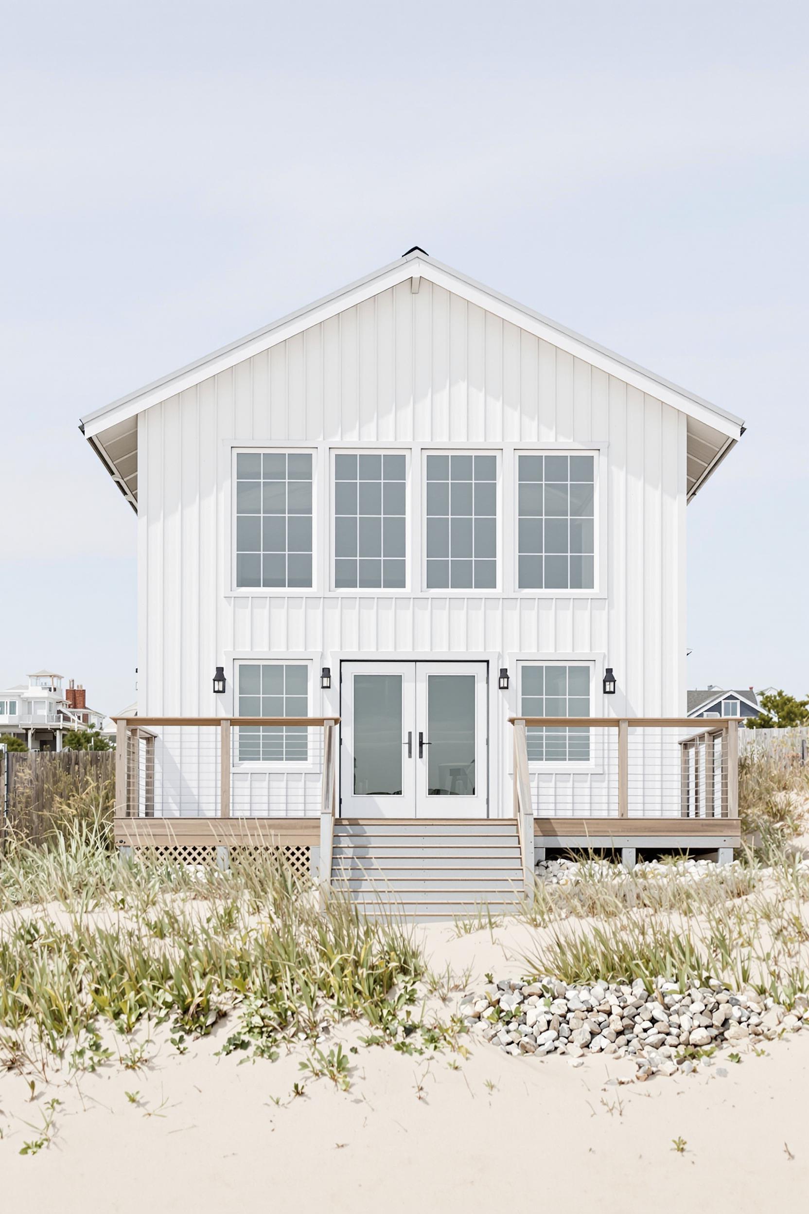 White beach house with large windows and sandy path