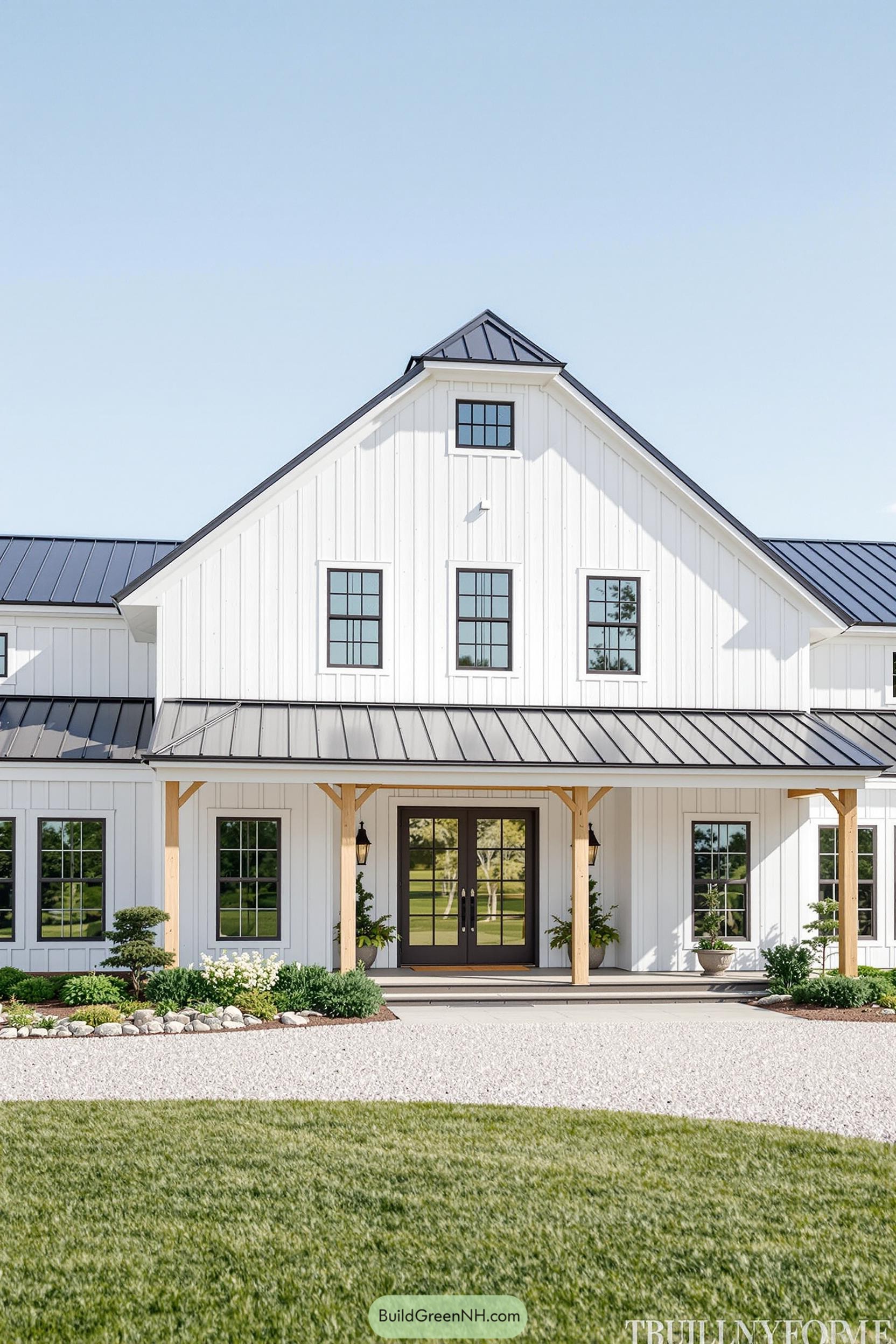 White barndominium with black roof and lush landscaping