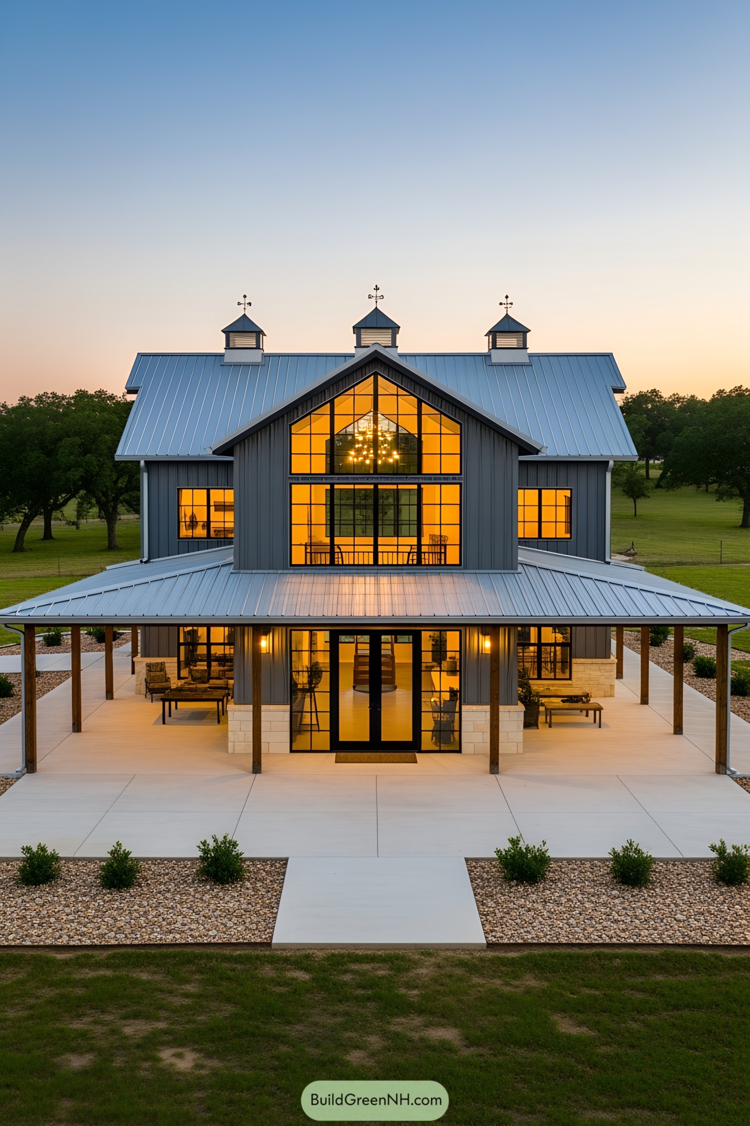 A modern barndominium with a wraparound porch at sunset