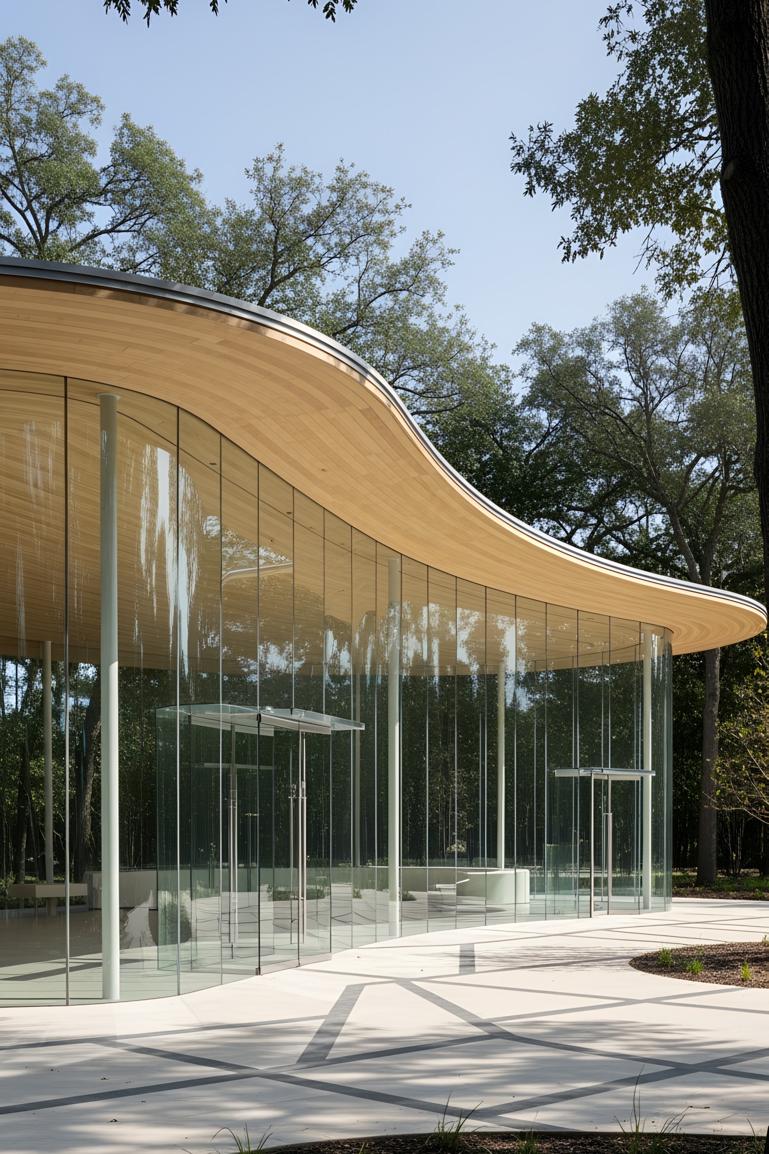 A glass pavilion with a wavy wooden roof surrounded by trees