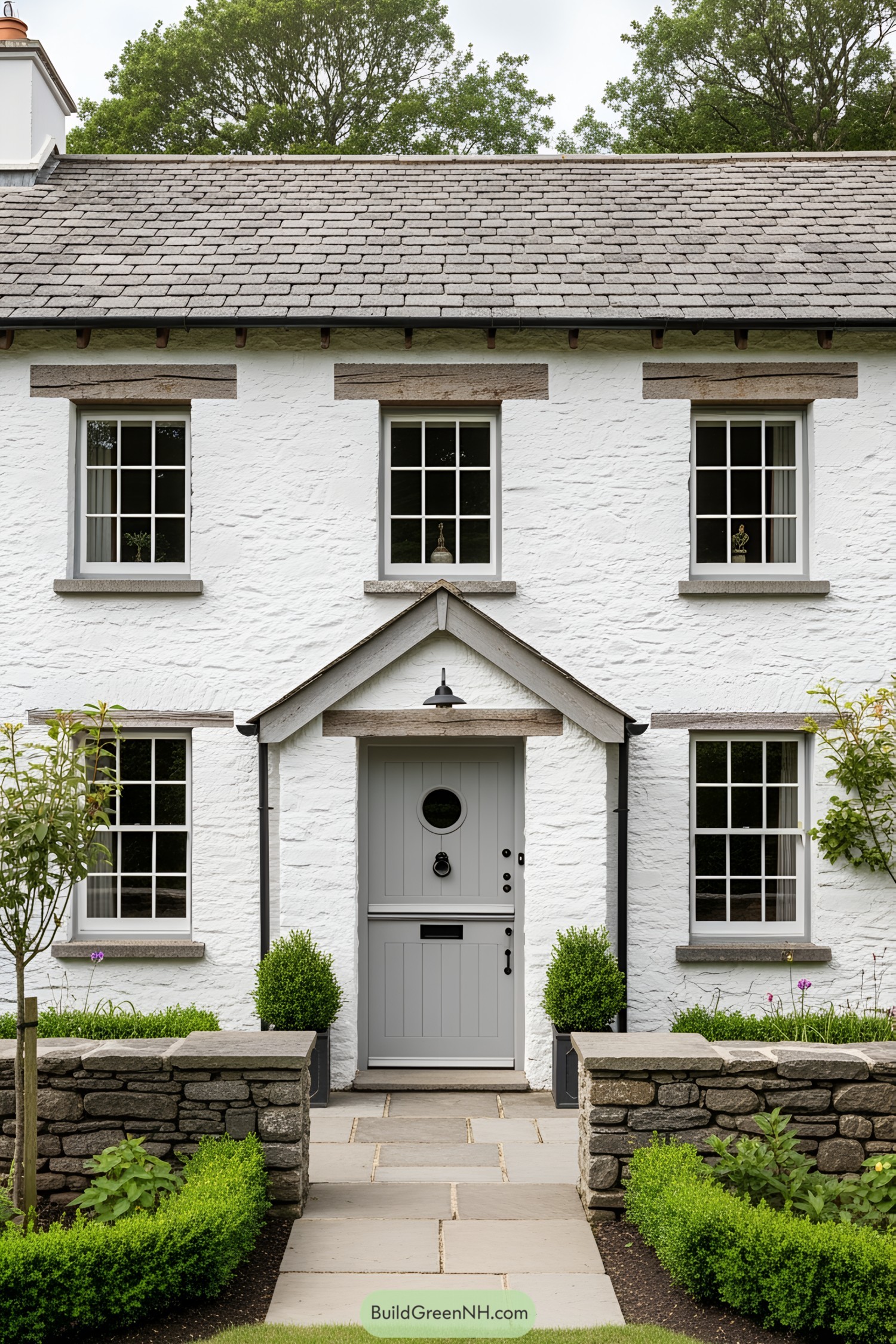 Charming white stone house with a grey door and lush greenery