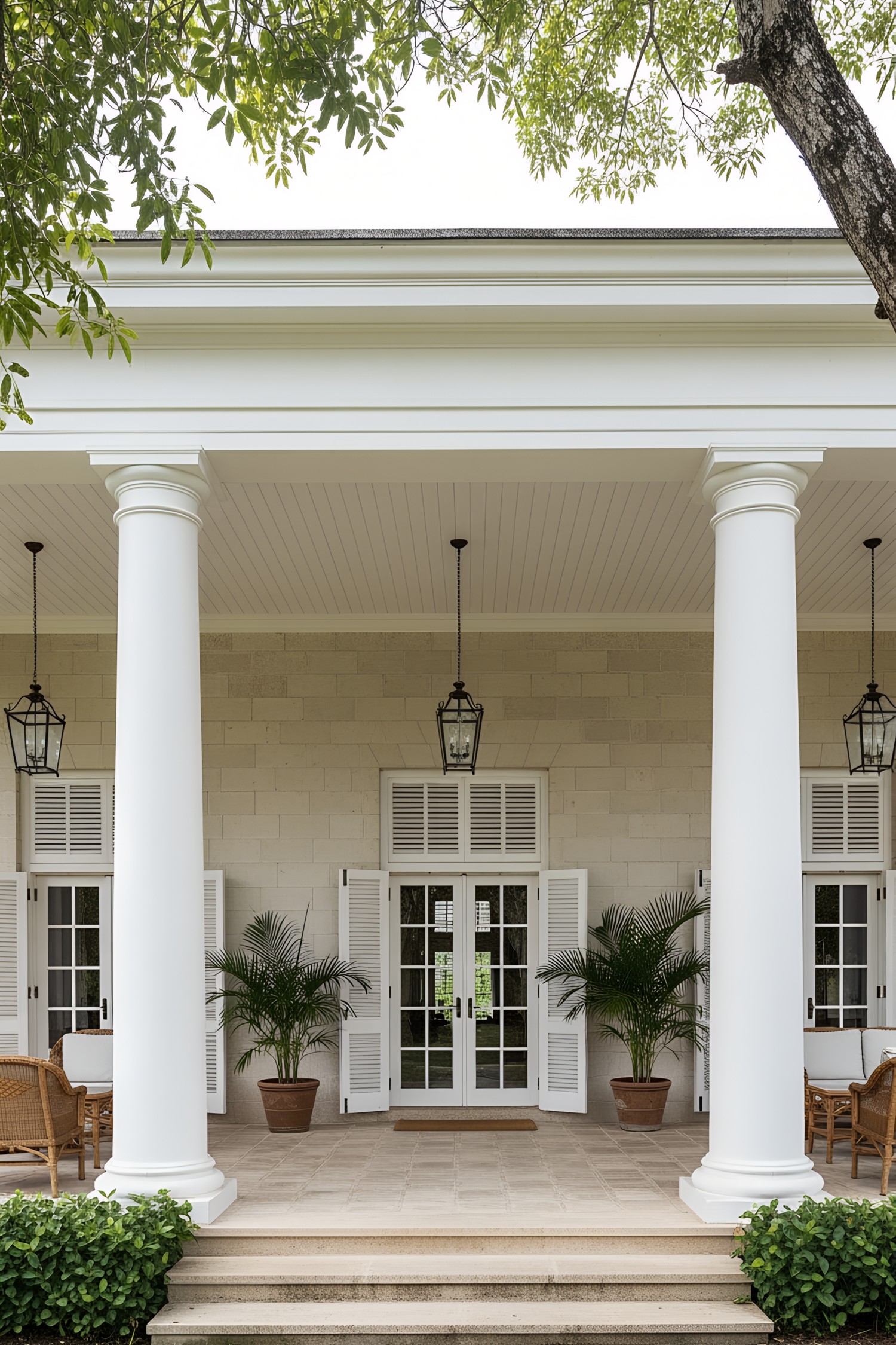 Front porch of a colonial house with large columns and potted plants