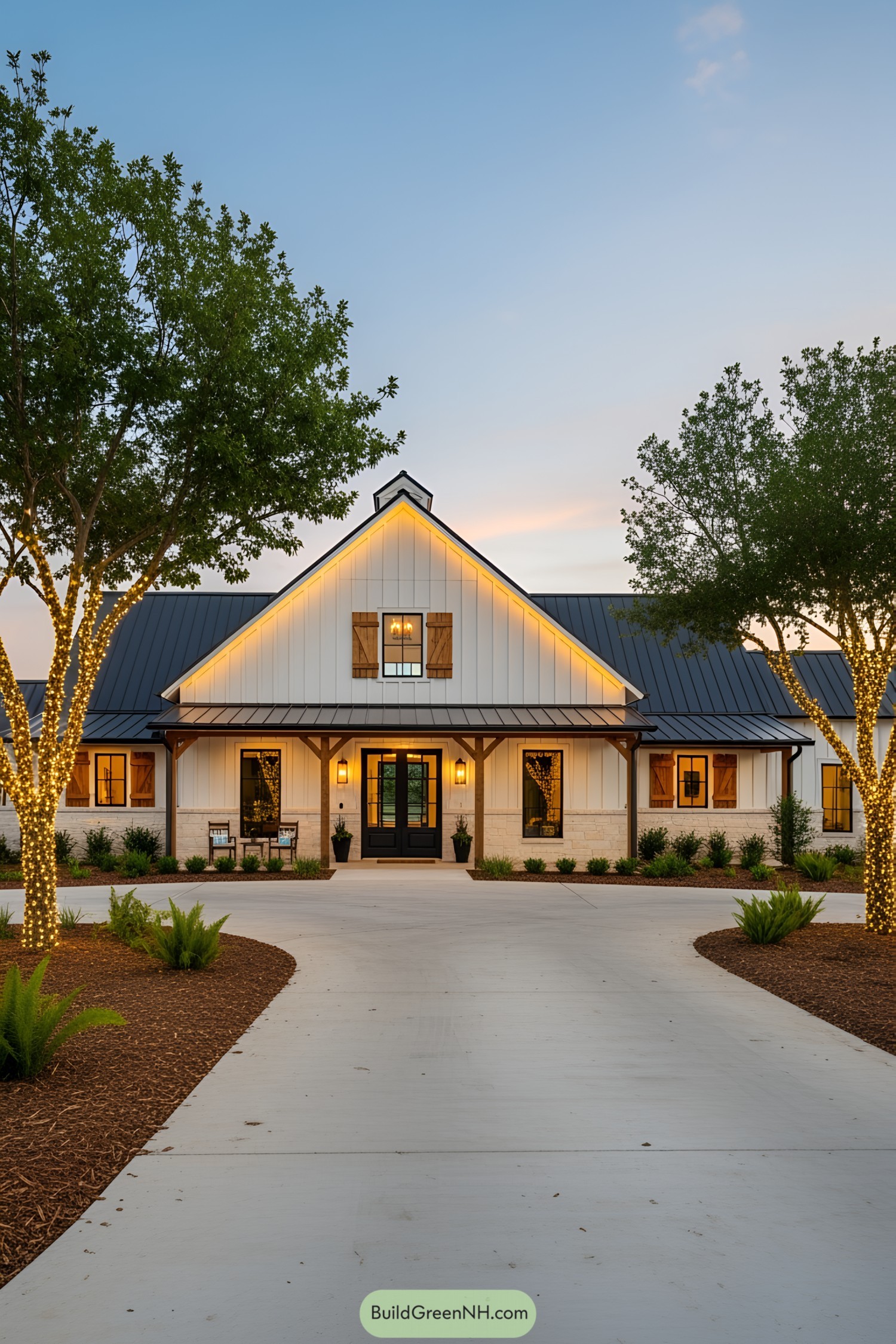 Modern barndominium framed by lit trees at sunset