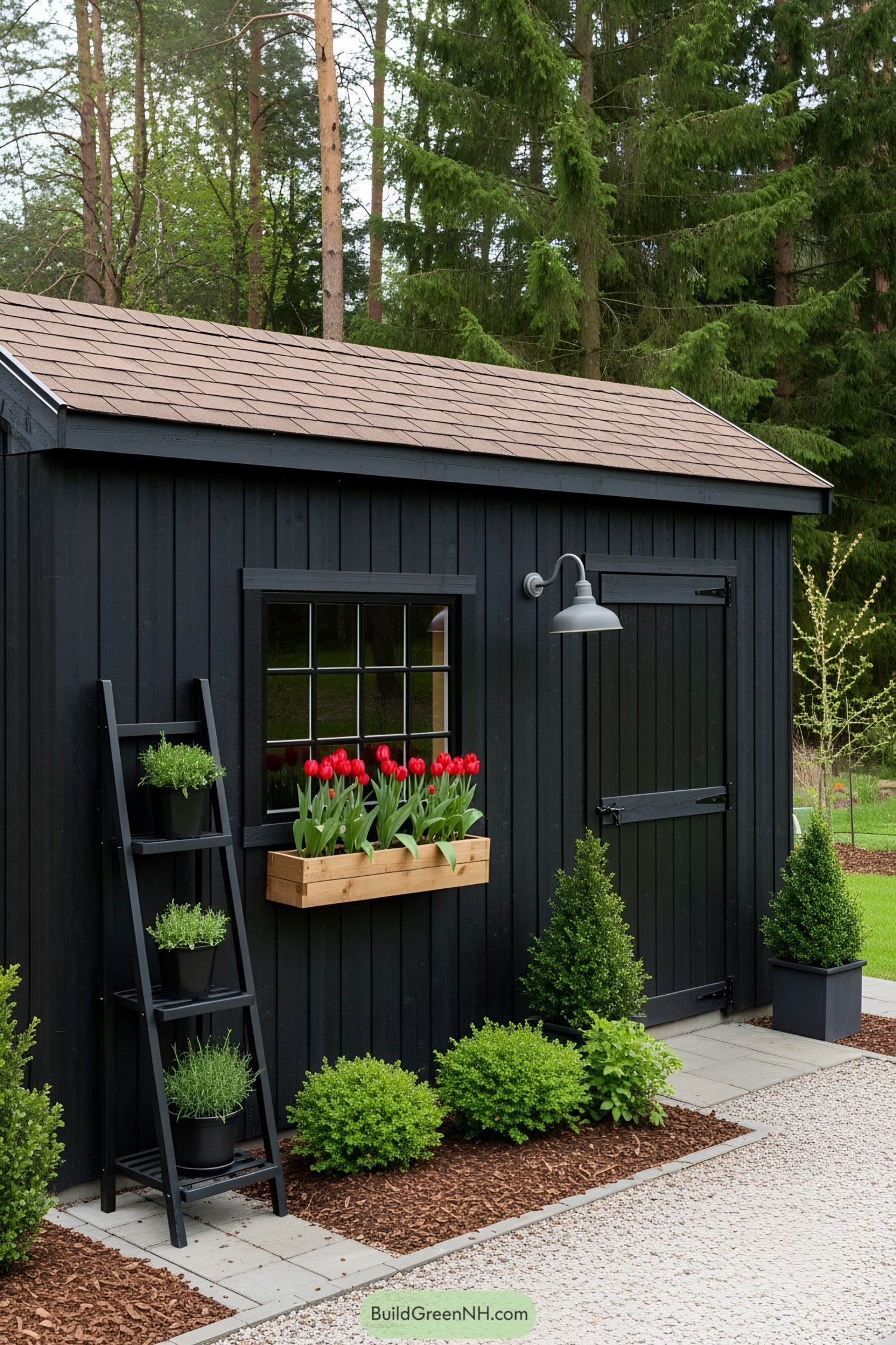 A black shed surrounded by greenery and red flowers