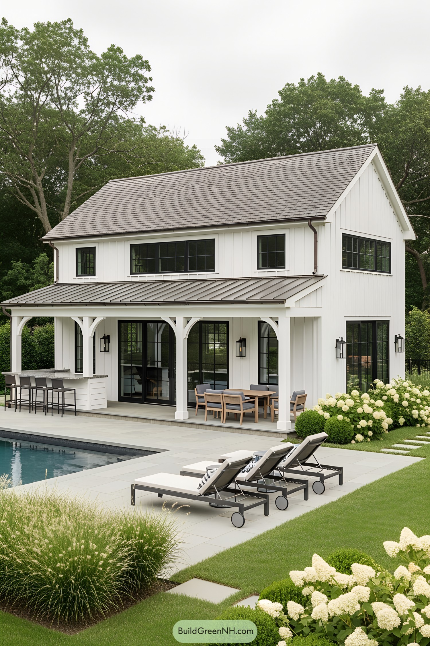 White farmhouse pool house with patio and lounge chairs by the water