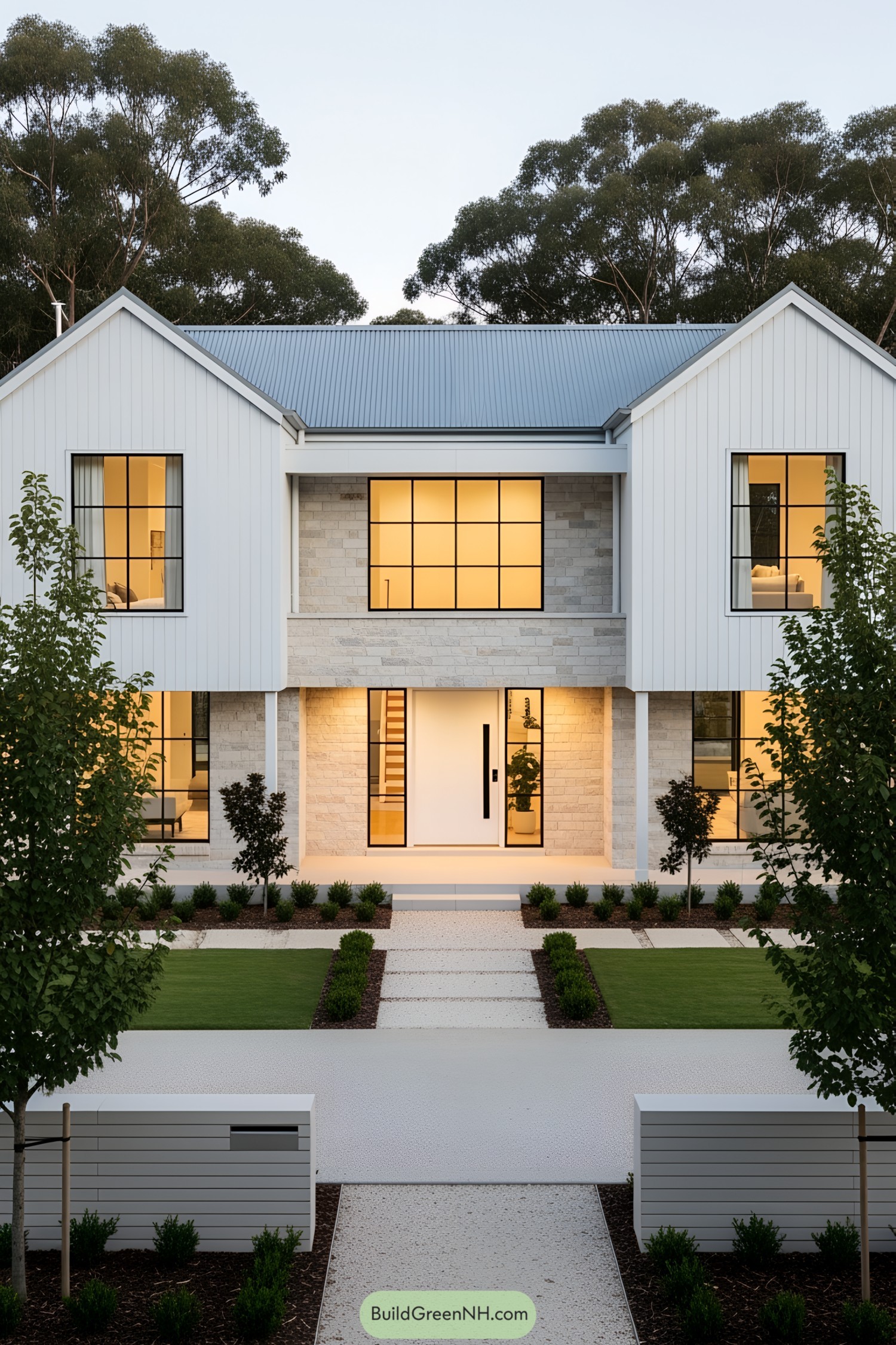 Modern farmhouse with lit windows, surrounded by greenery