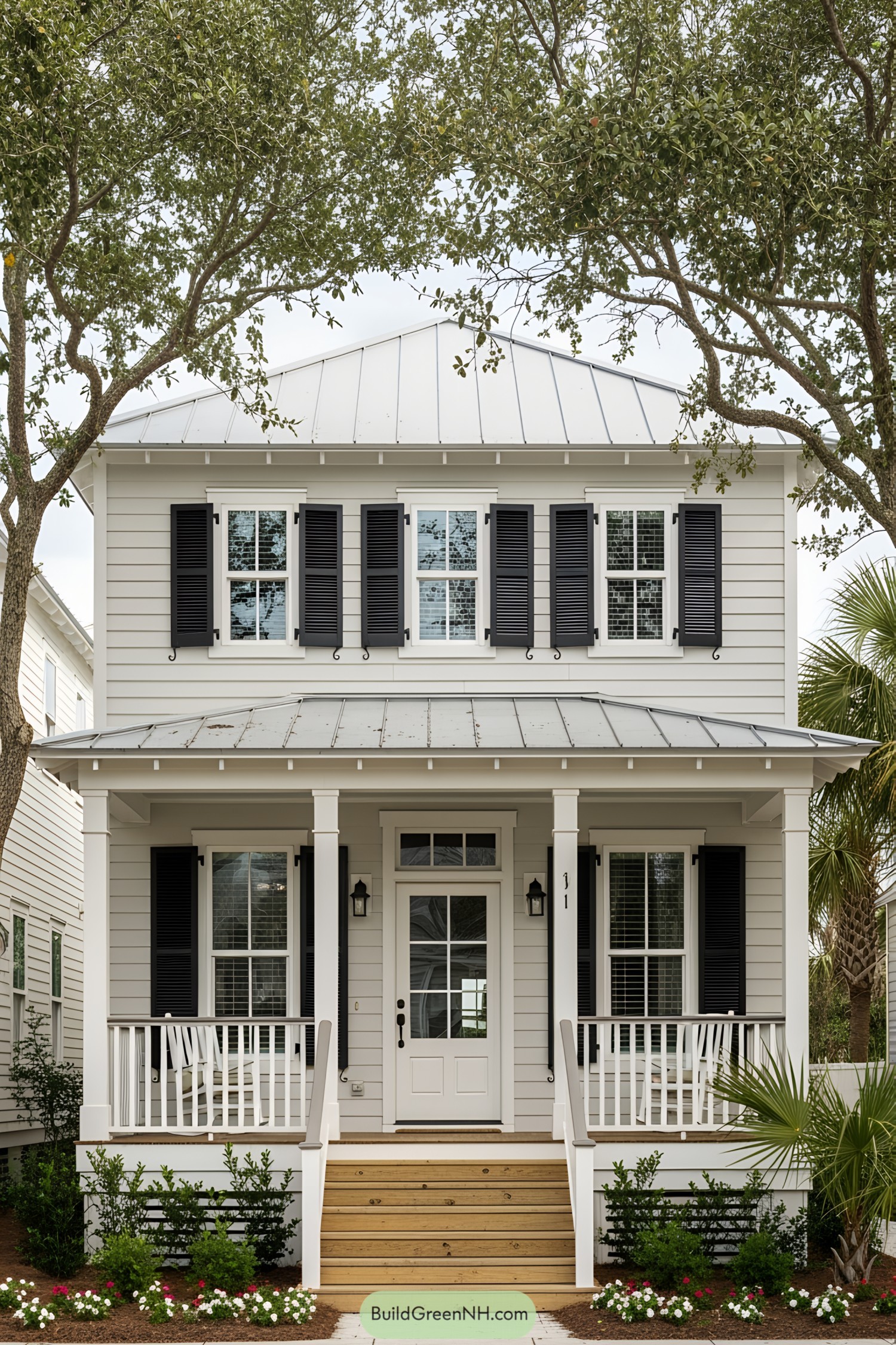 White two-story beach house with black shutters under trees