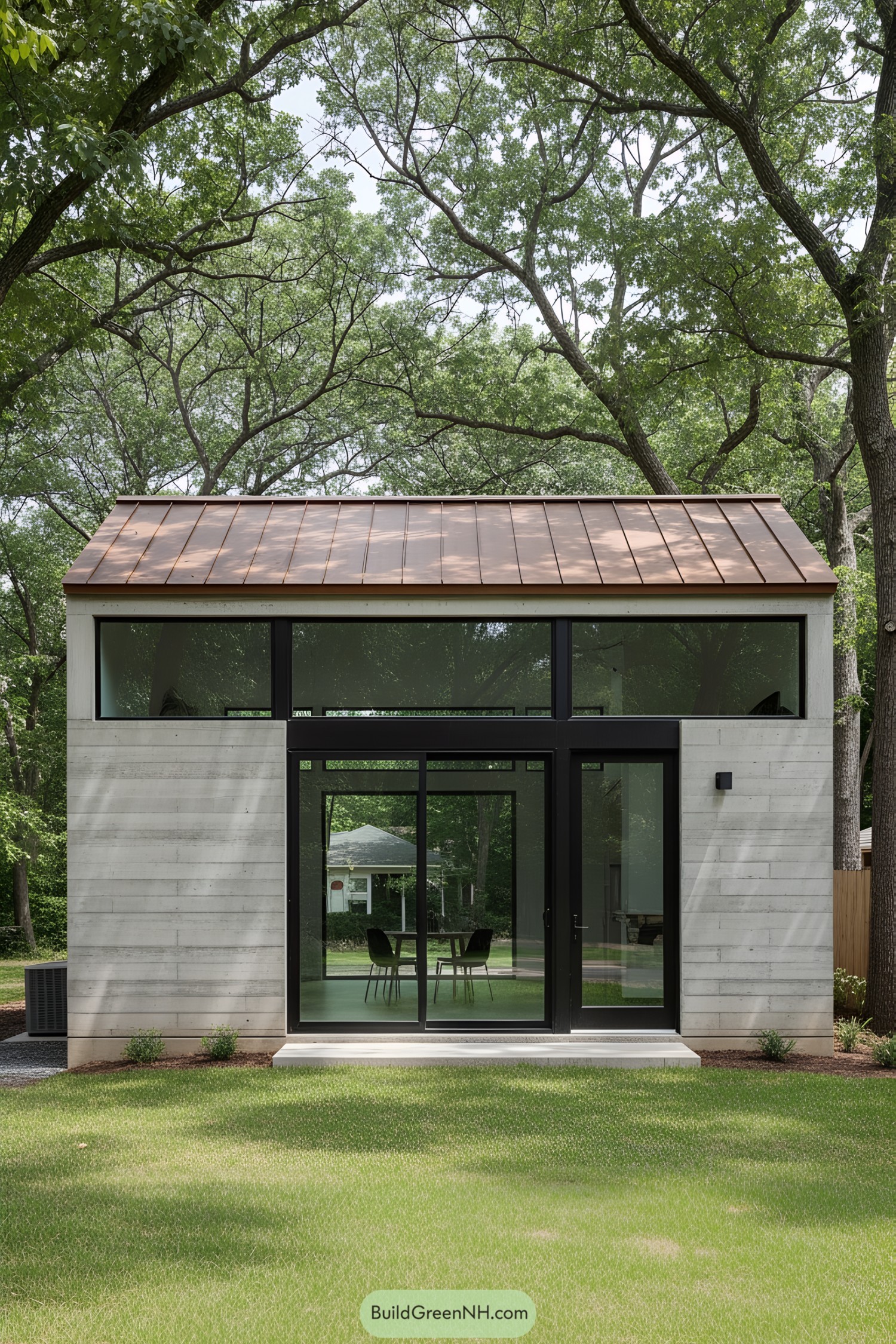 Small concrete house with glass doors and metal roof under large trees