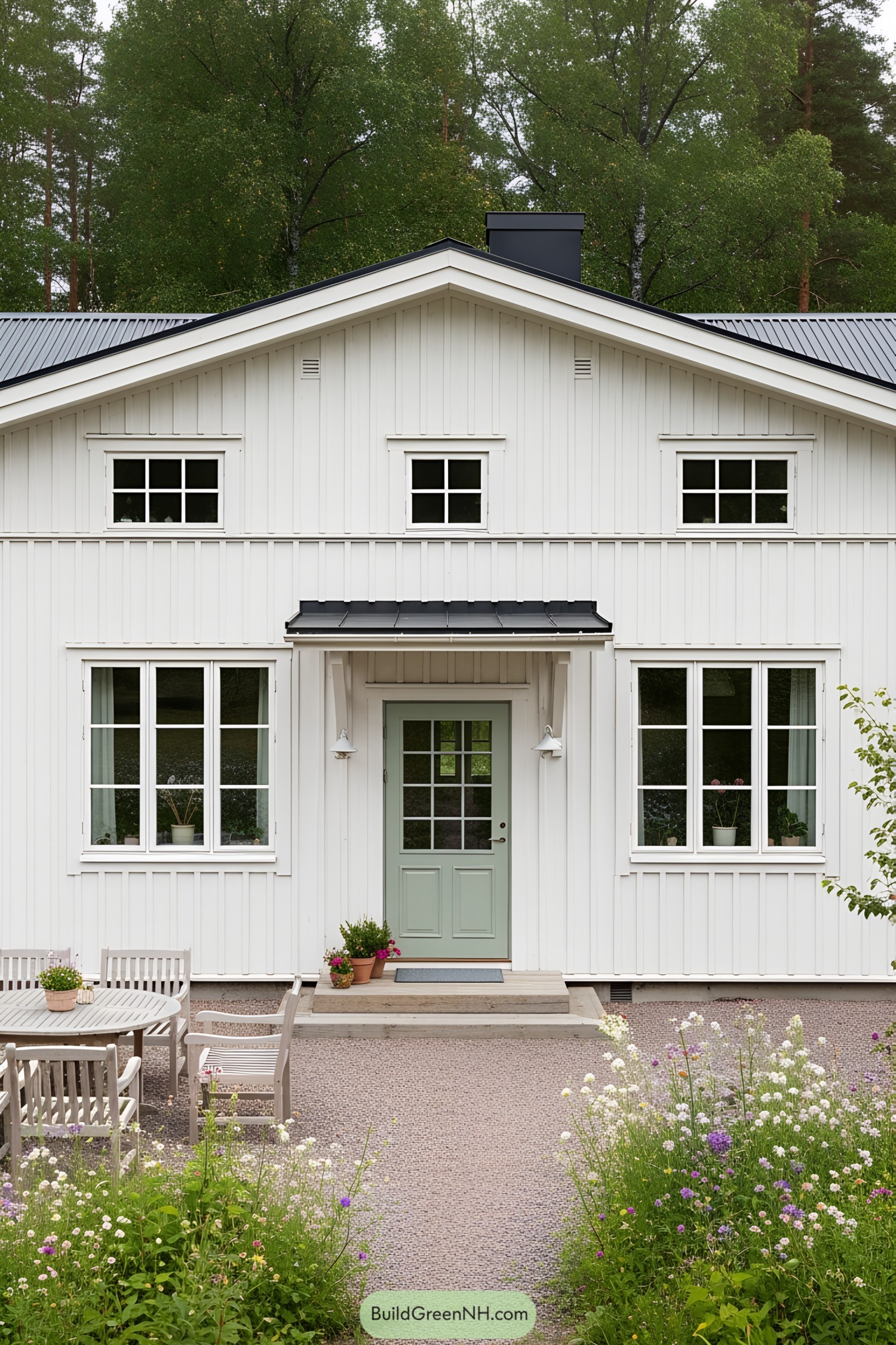 White painted farmhouse with a green door surrounded by wildflowers