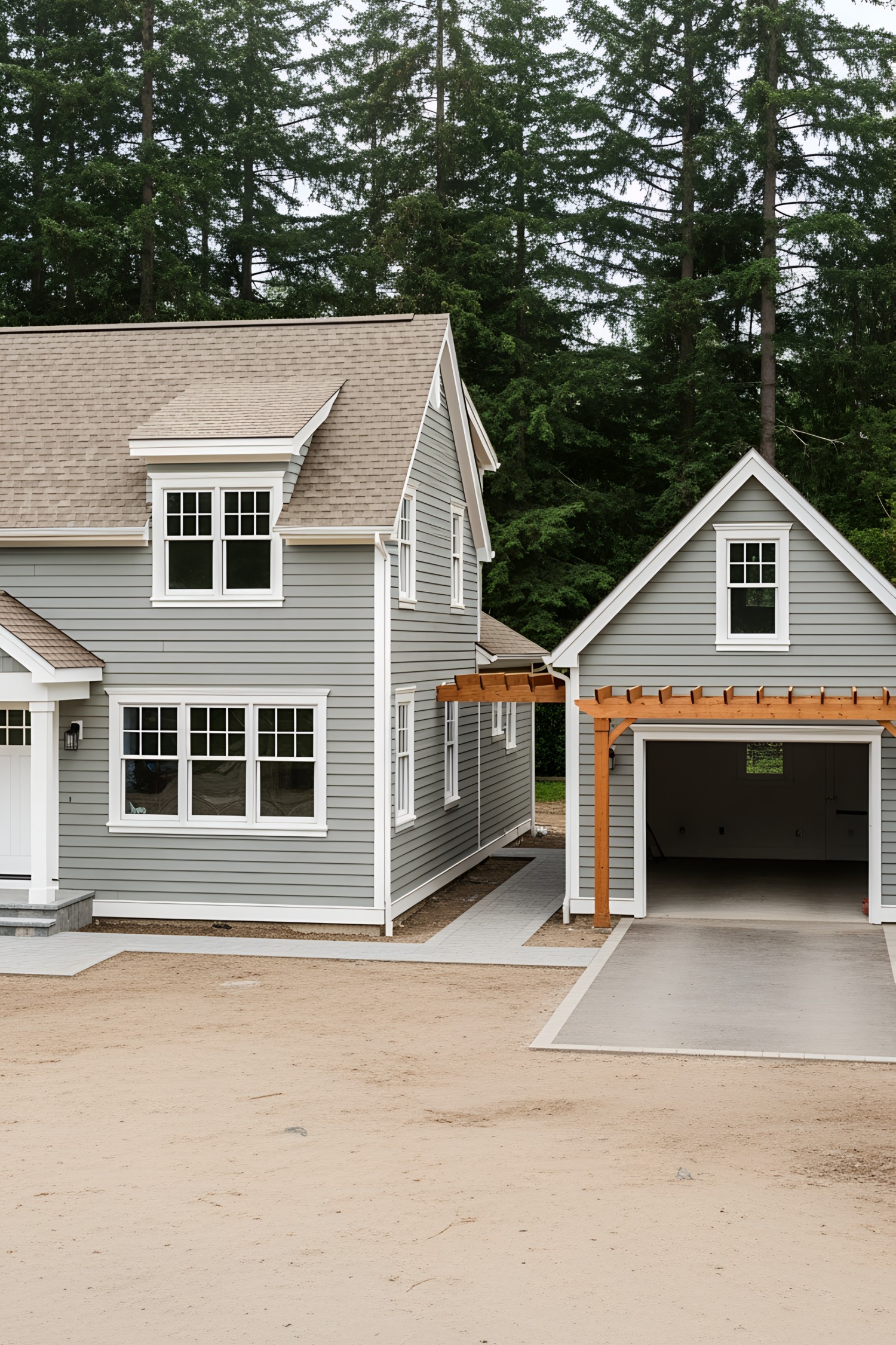 Gray cottage with a connected garage surrounded by tall trees