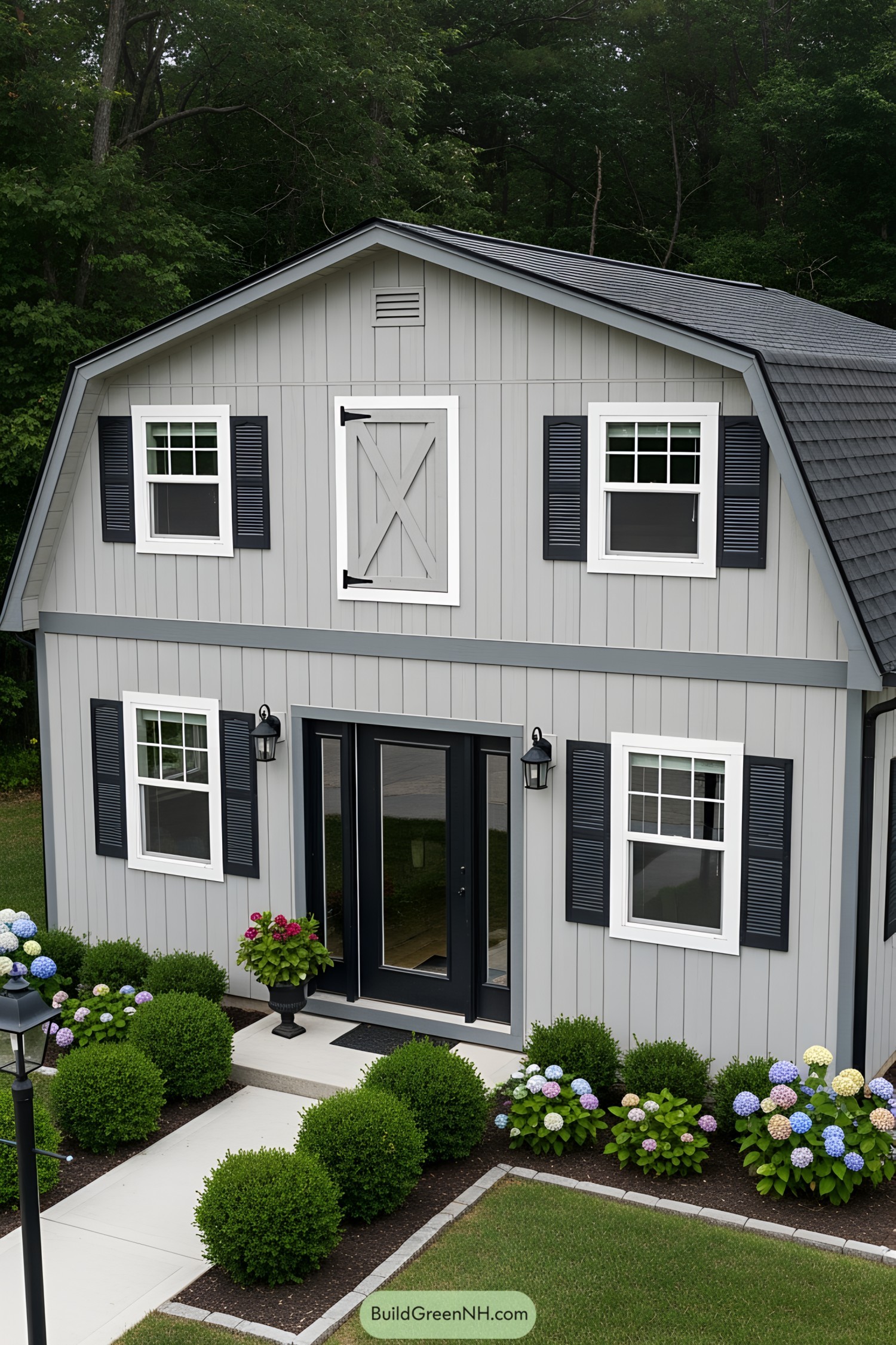 A compact gray barn-style house with black shutters and flowerbeds