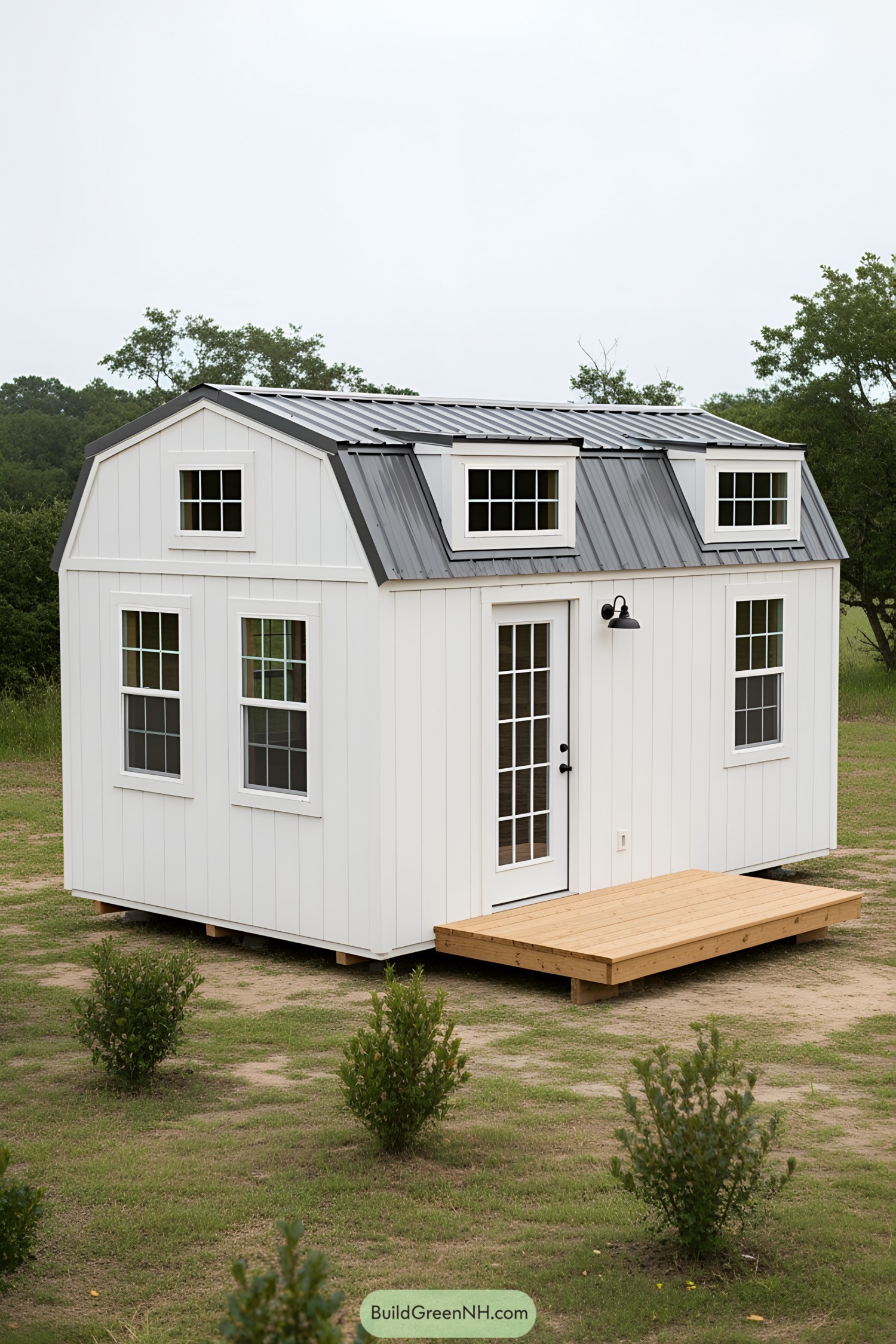 White barn-style tiny house with gray roof and wooden deck