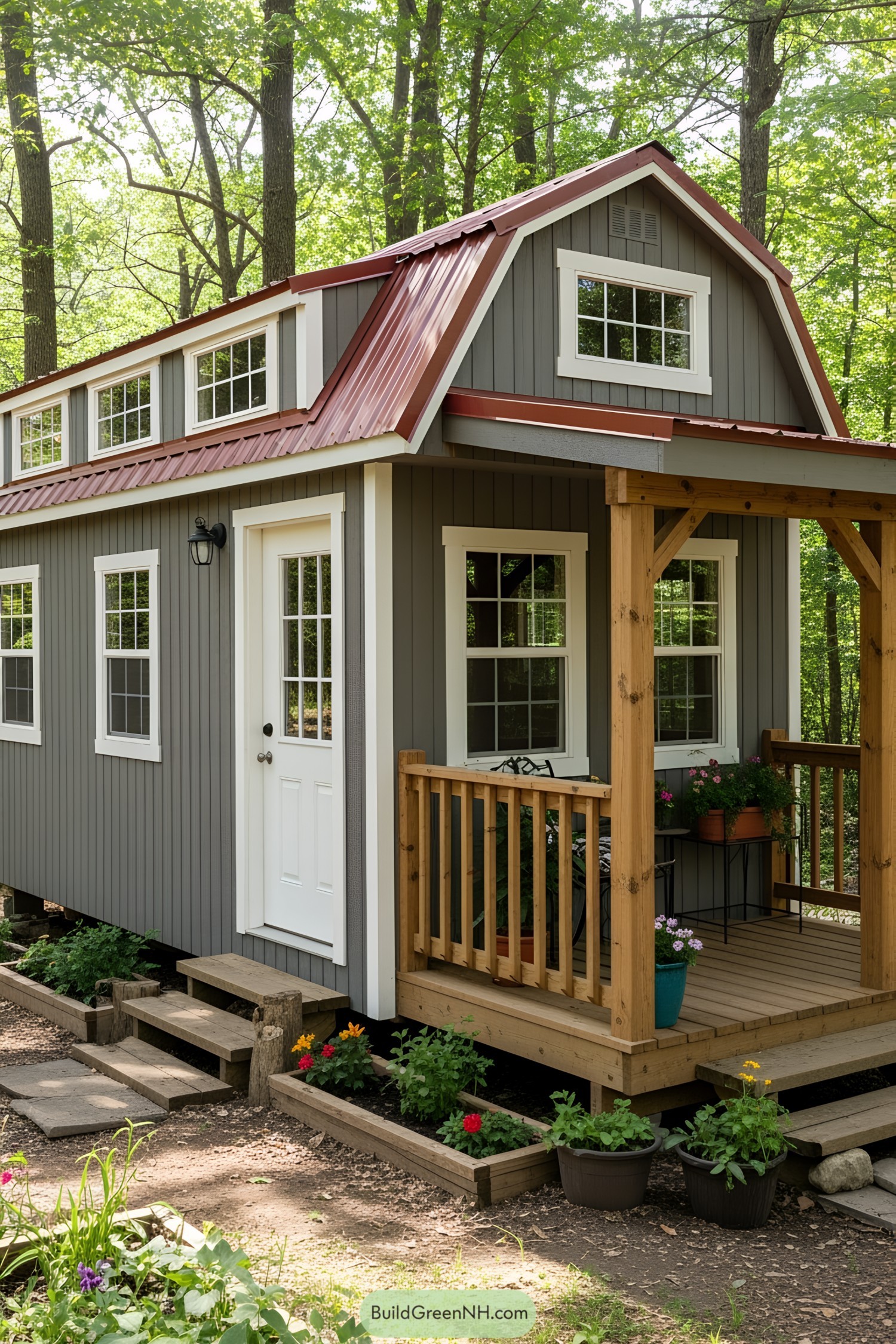 A quaint gray barn-style tiny house with a red roof and cozy porch