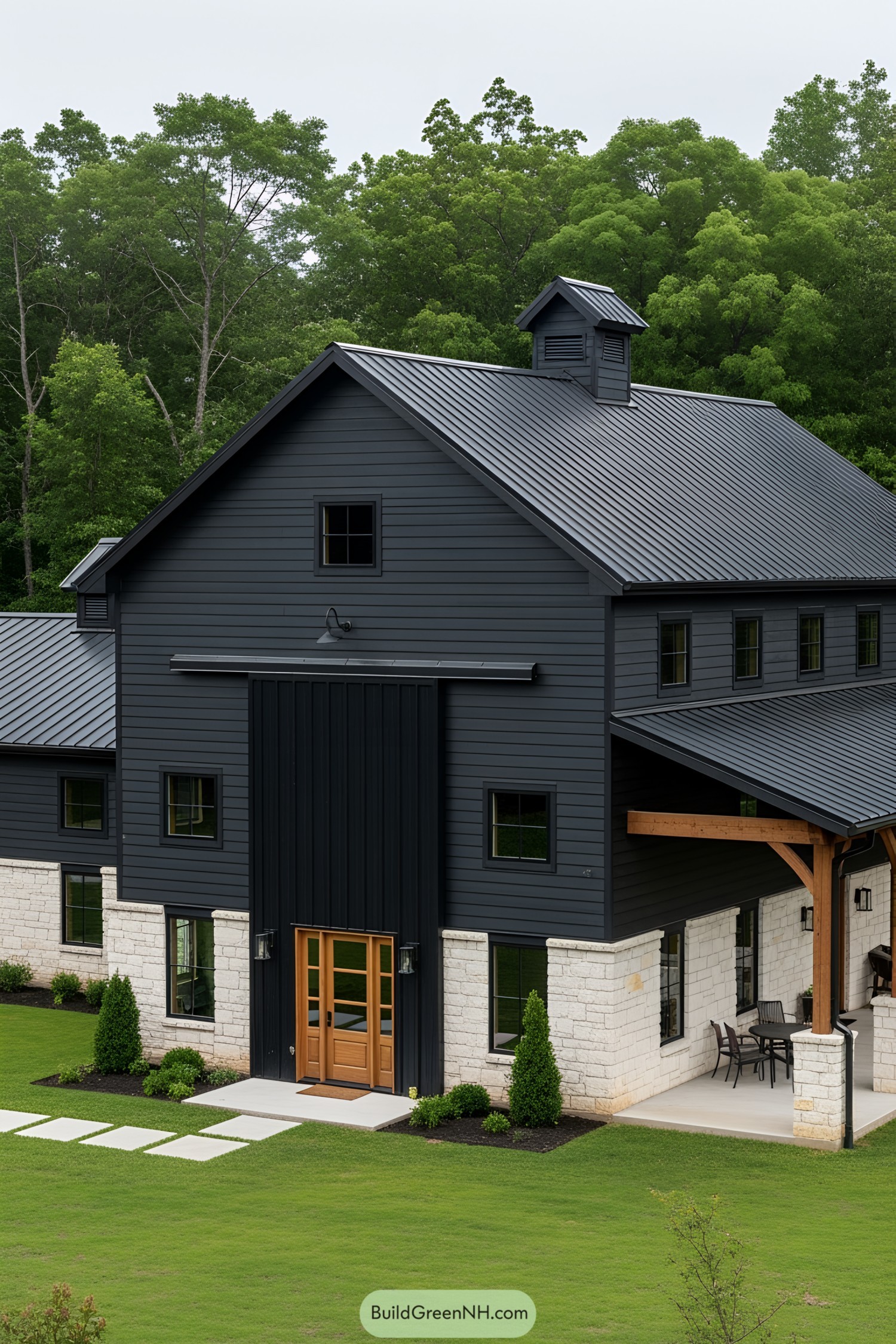 Black barndominium with stone accents surrounded by greenery