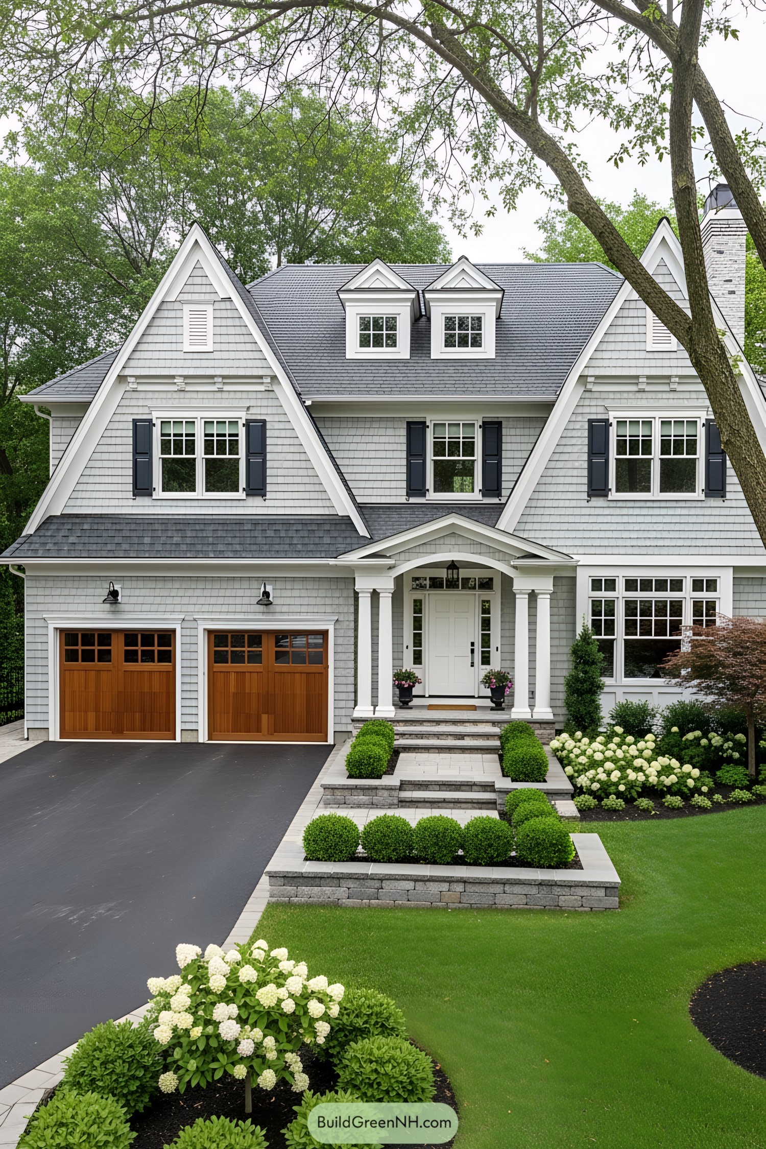 Charming blue-gray house with wooden garage doors and lush landscaping
