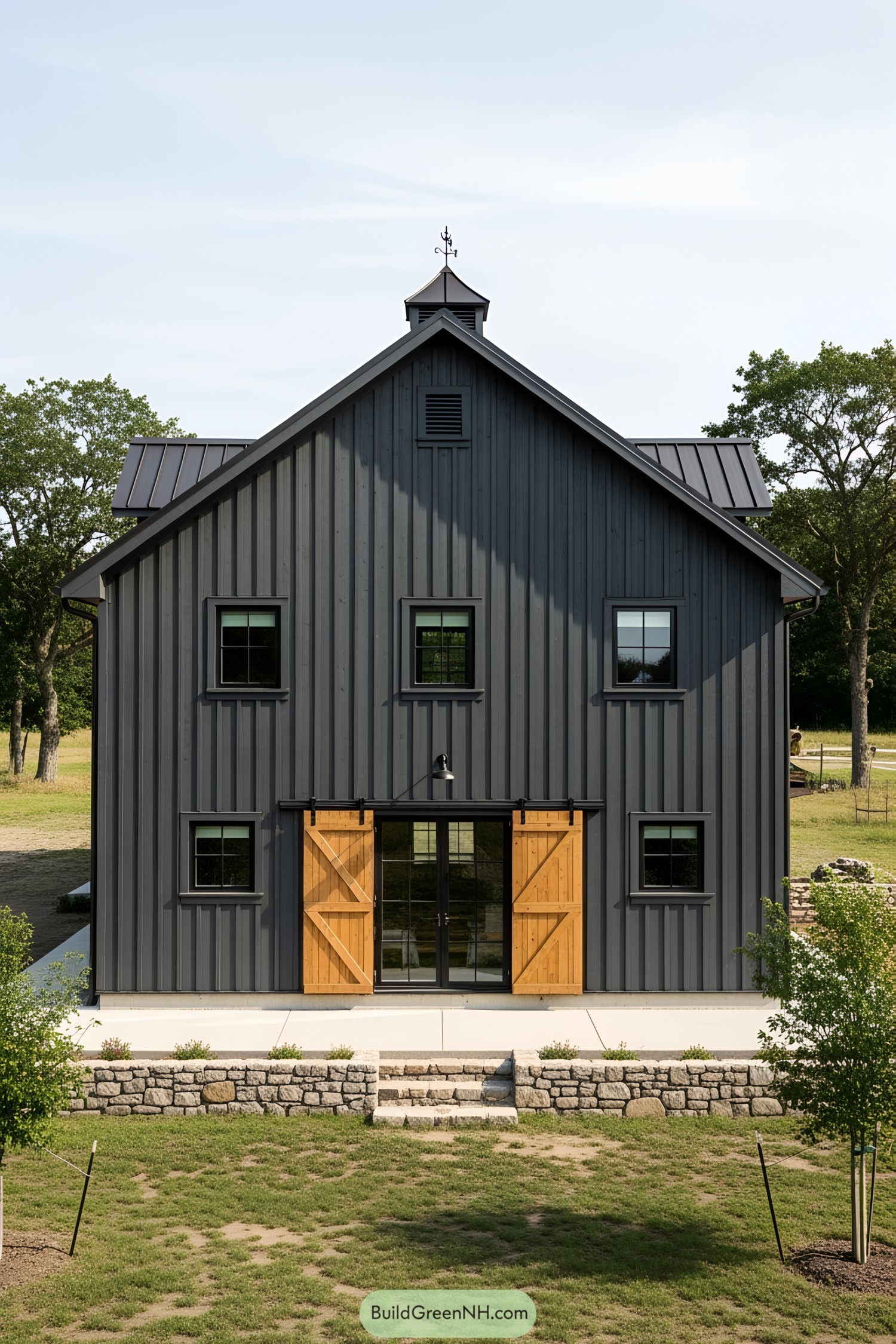 Dark gray barn house with wooden doors and a small, lush garden