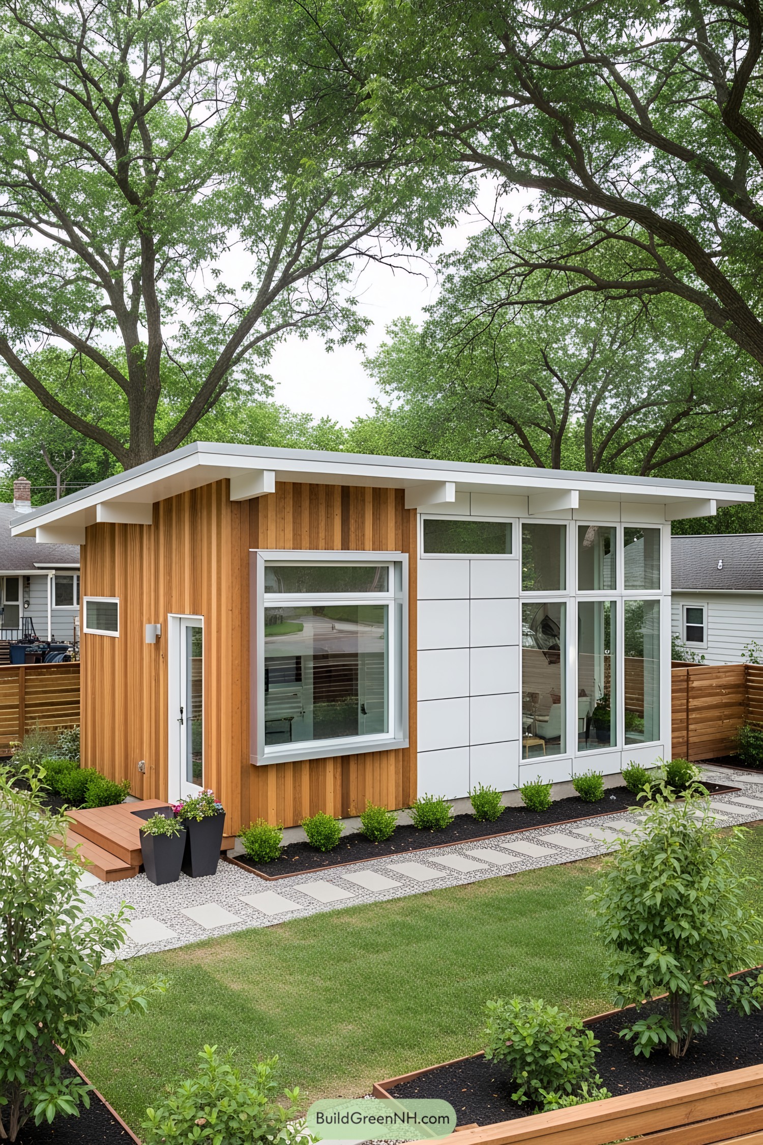 Small wooden and white-panel house surrounded by lush green garden and trees