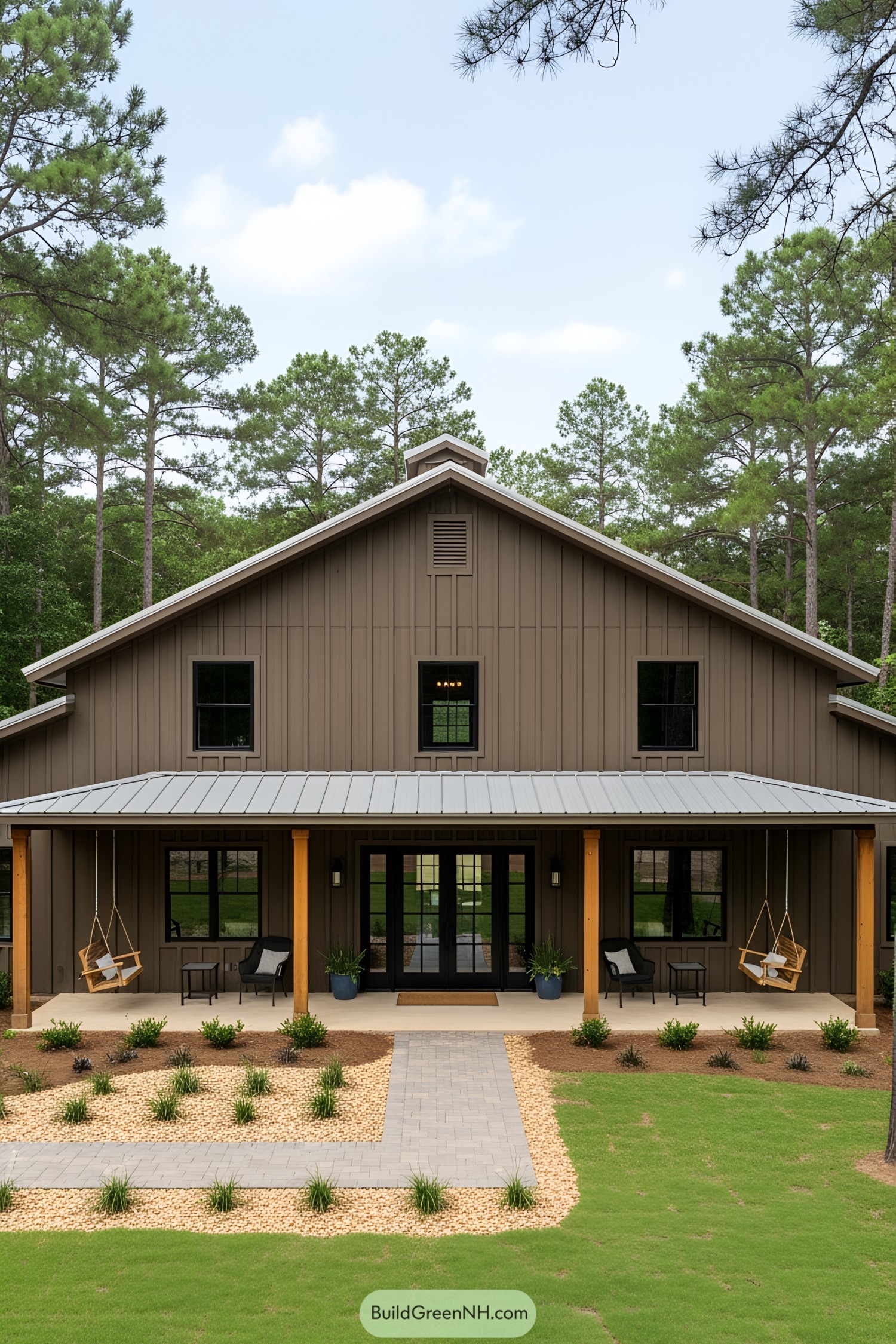 A barndominium with a wide porch and wooden columns, nestled among tall trees