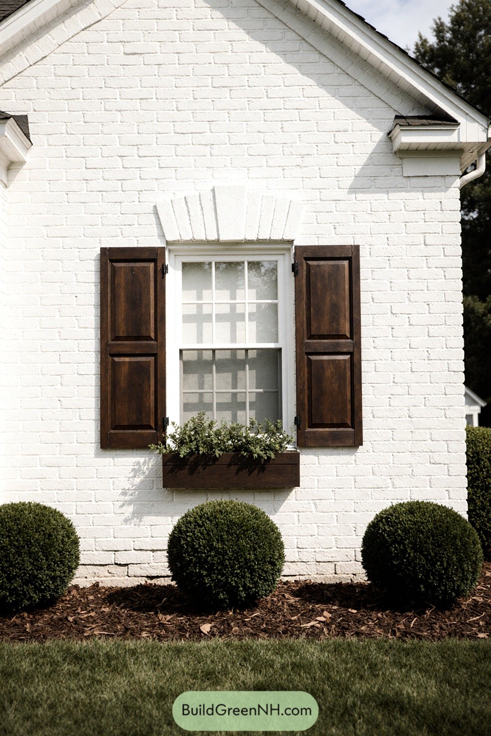 White brick house with dark wooden shutters and shrubs