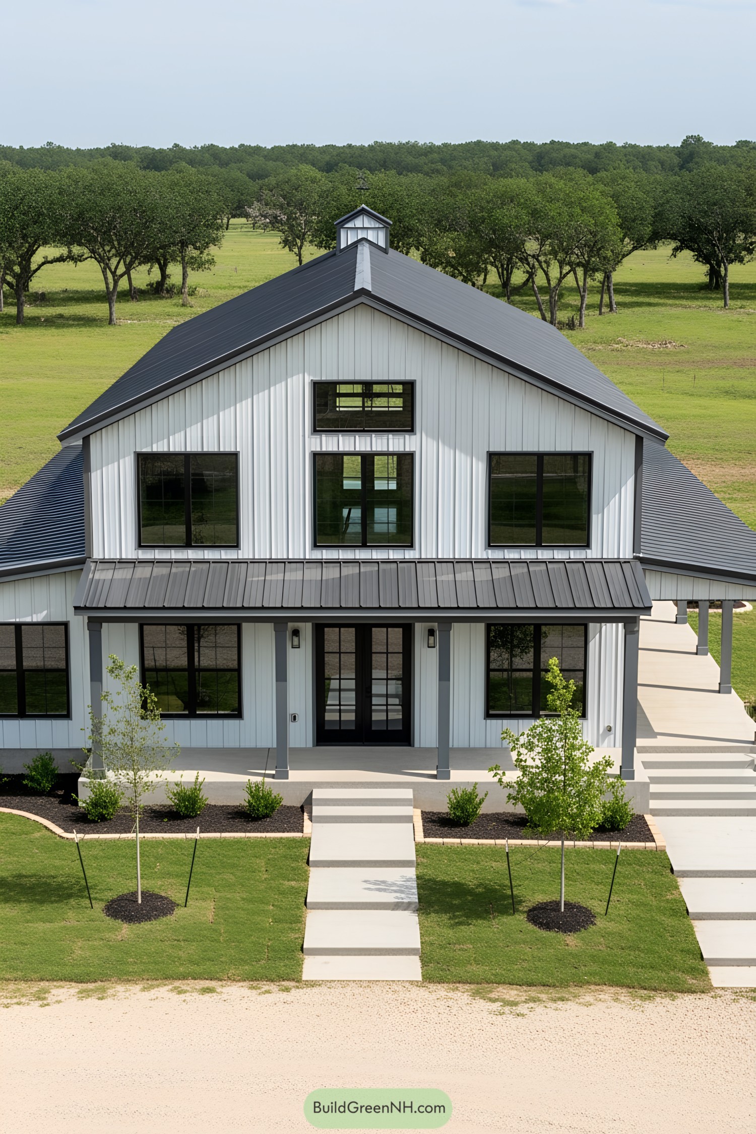 White barndominium with black roof and large windows in a grassy field