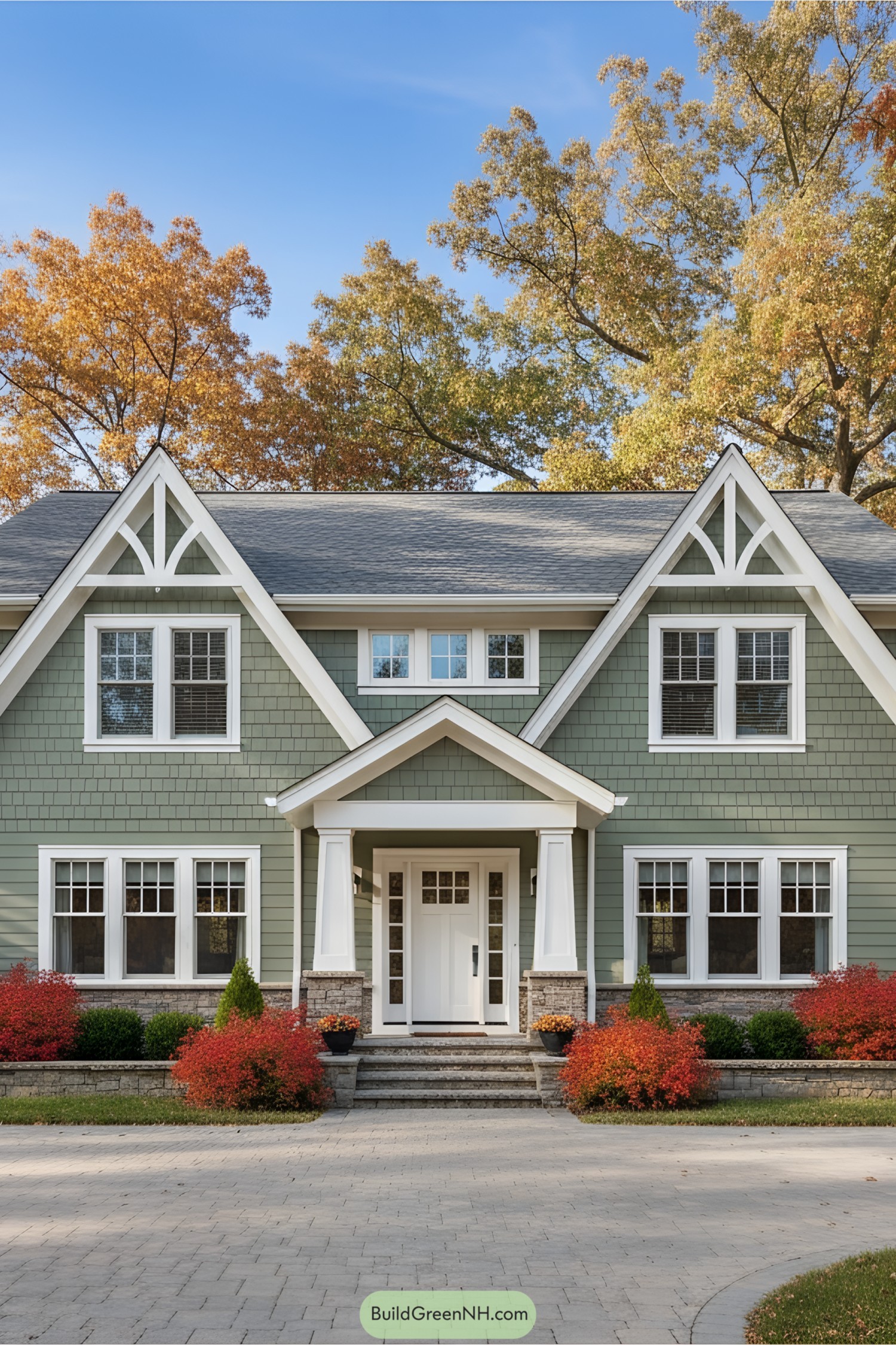 Green suburban house surrounded by fall foliage and clear blue sky