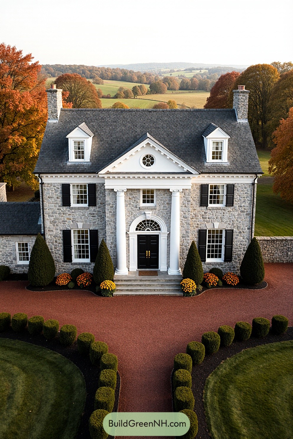 Stone colonial house with red driveway amidst fall foliage