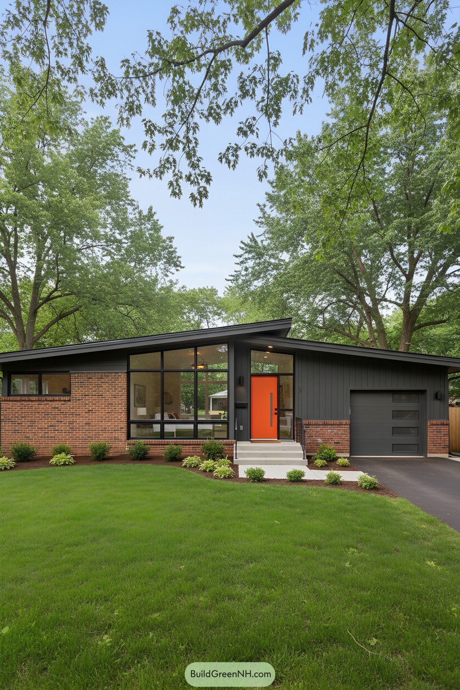 Brick ranch house with large windows and an orange door, surrounded by trees and greenery