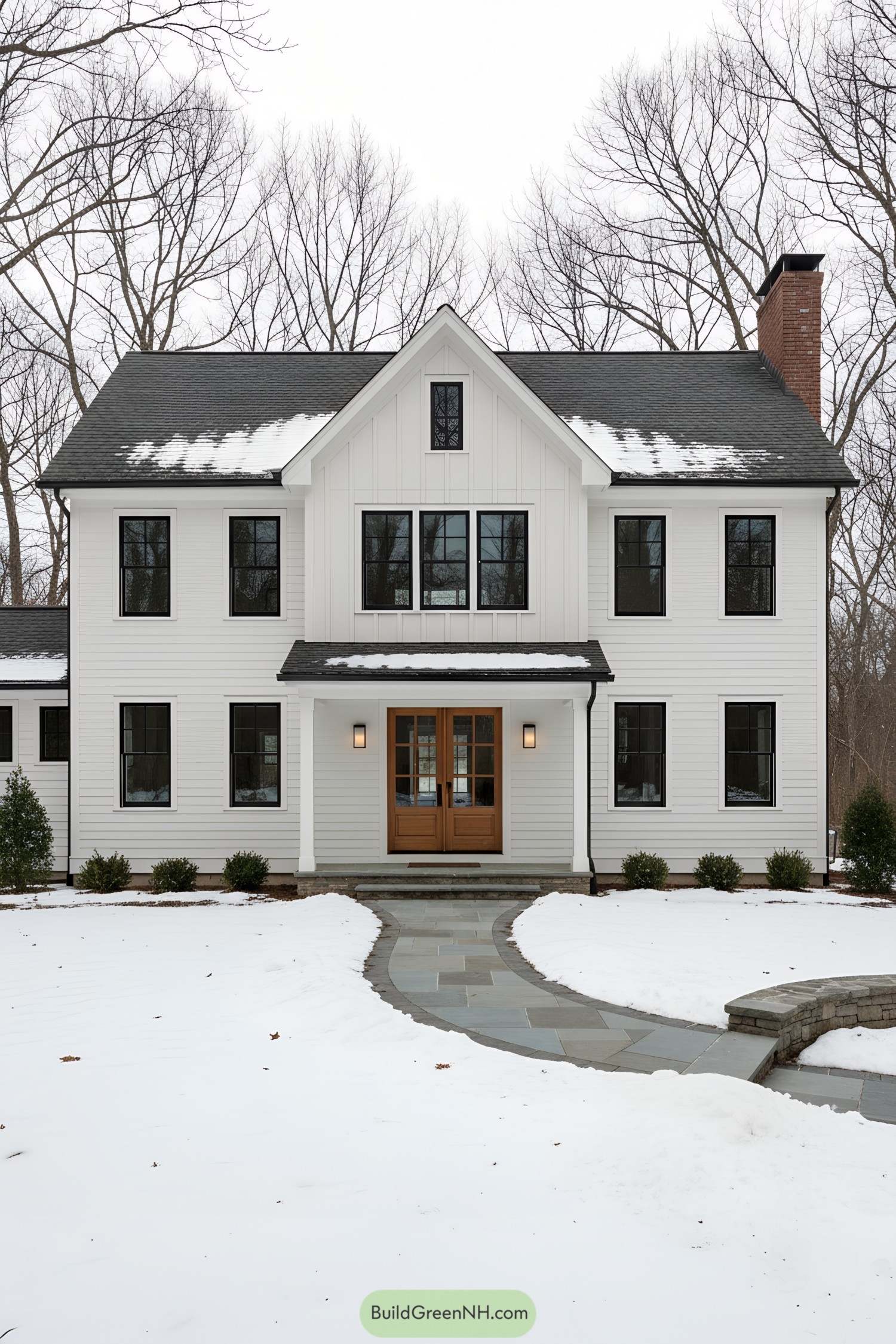 White modern colonial with central gable, black windows, and oak double door in winter