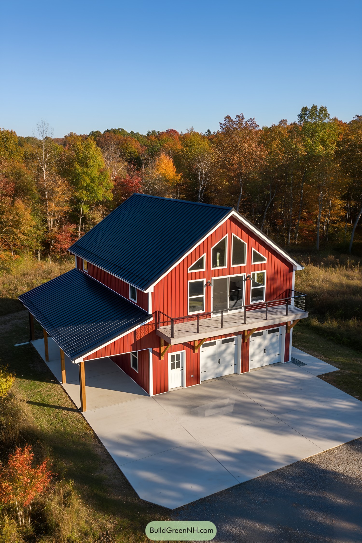 Red metal barn house with black gable roof, upper balcony, and twin garage doors