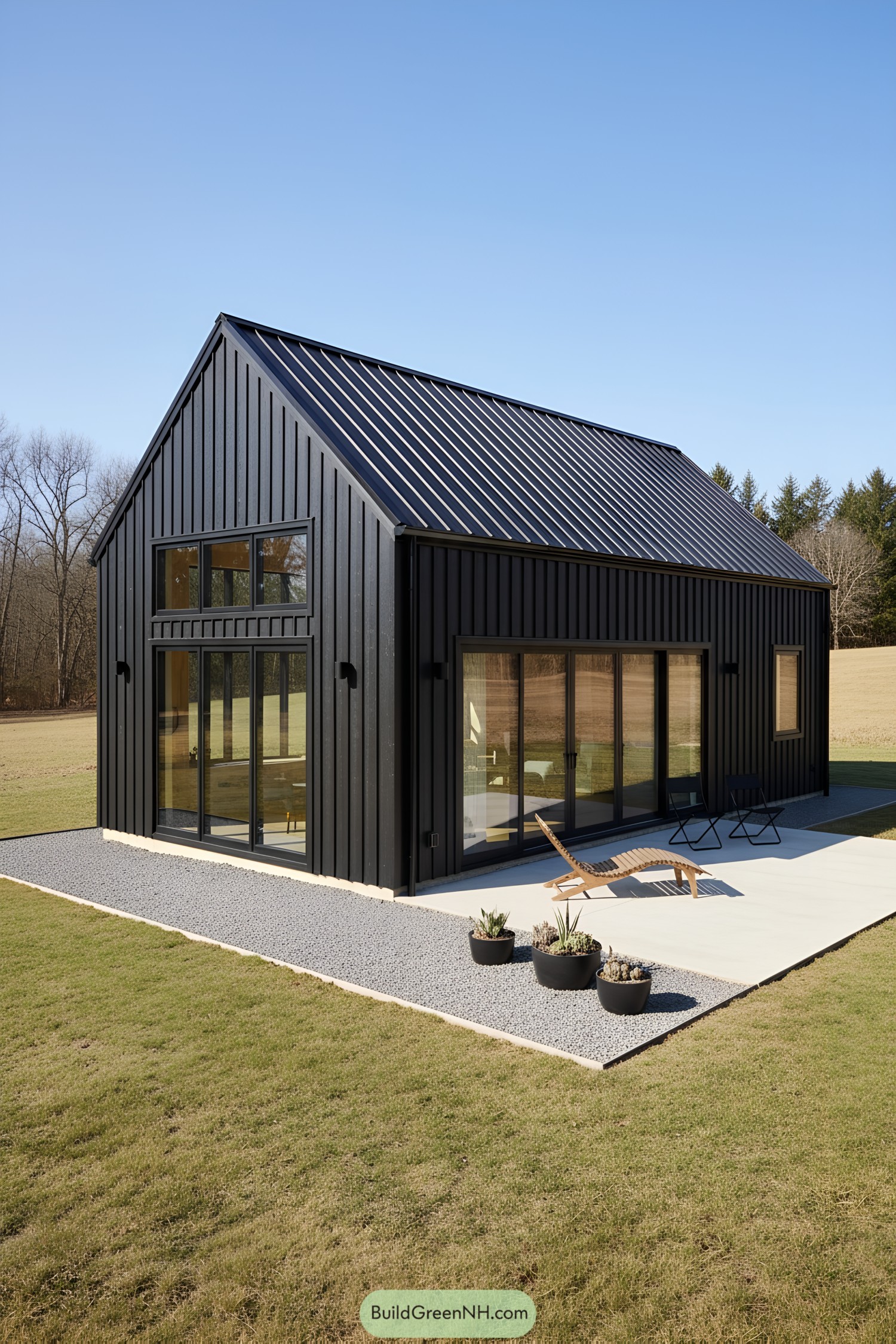 Modern black gabled barn with large glass doors opening to a concrete patio and gravel border