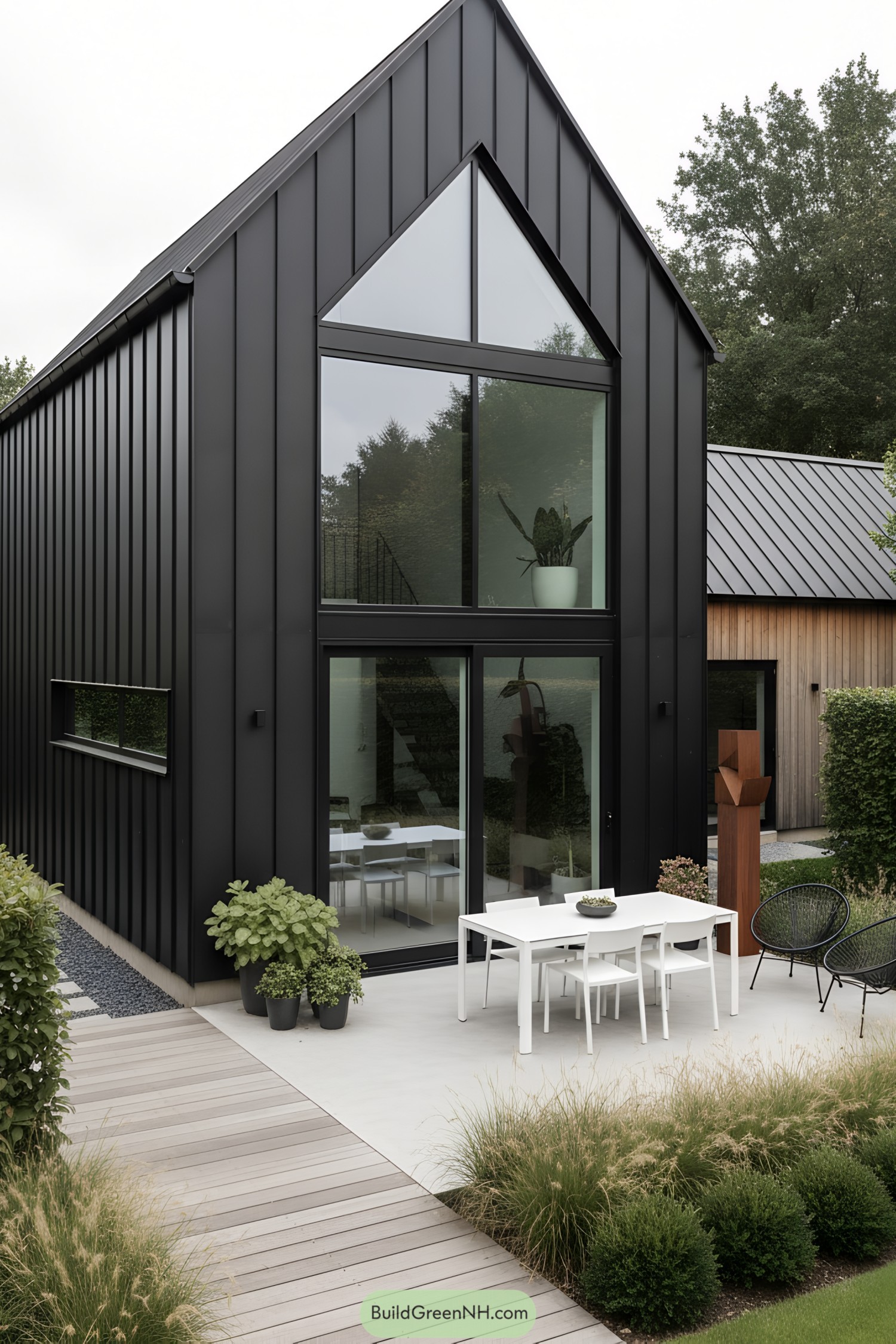 Black metal-clad barn with tall triangular glazing and minimalist patio furniture