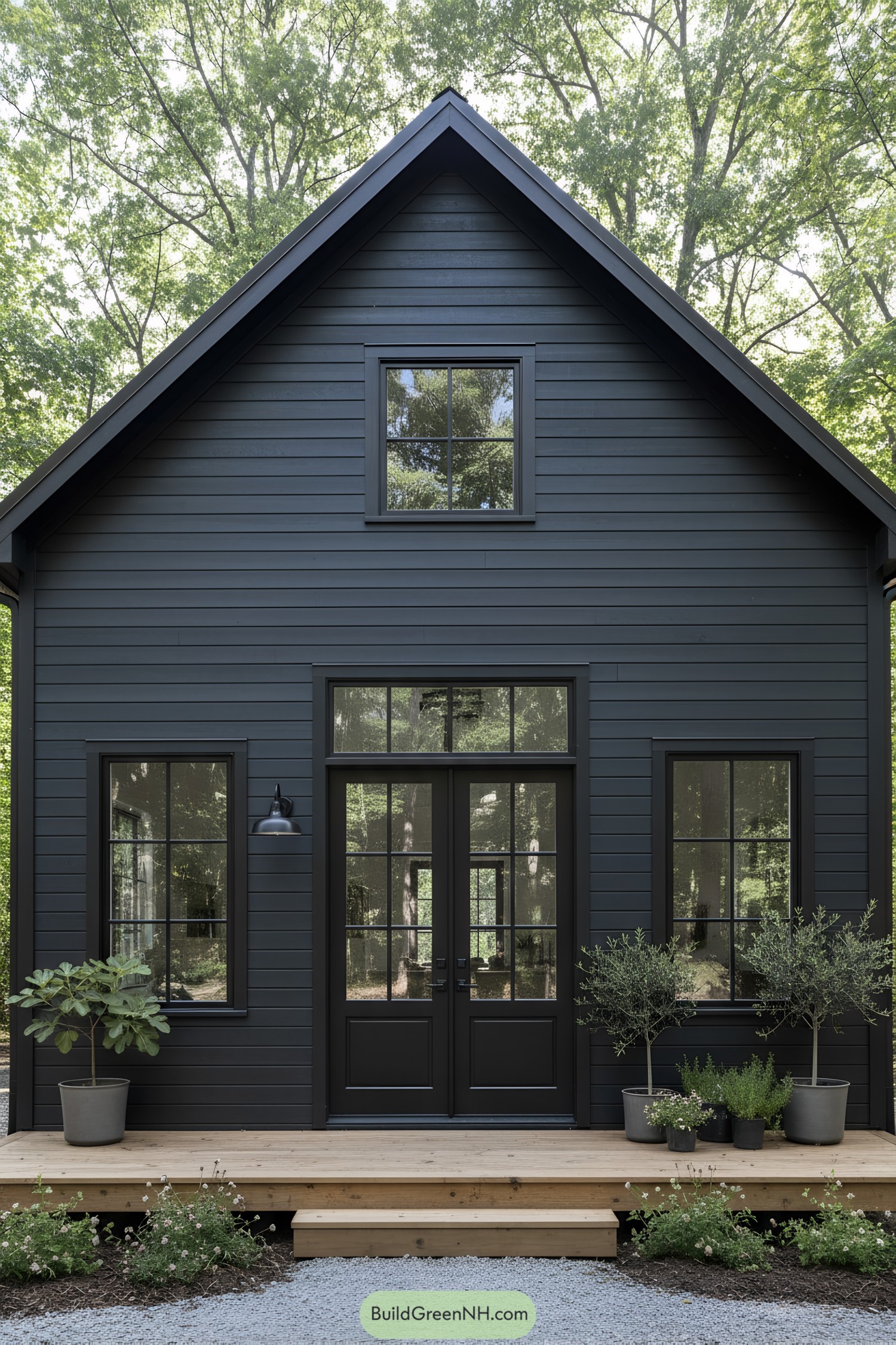 Black-clad gabled barn house with wood porch and potted greenery