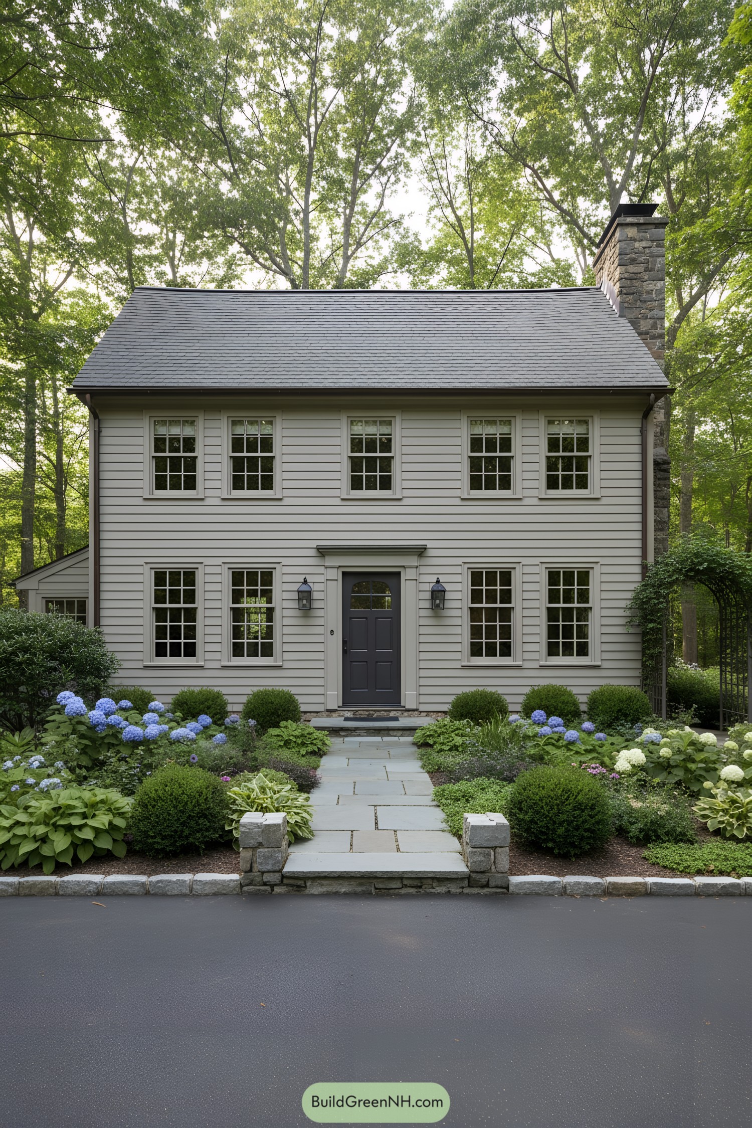 Two-story gray clapboard cottage with central door and stone chimney