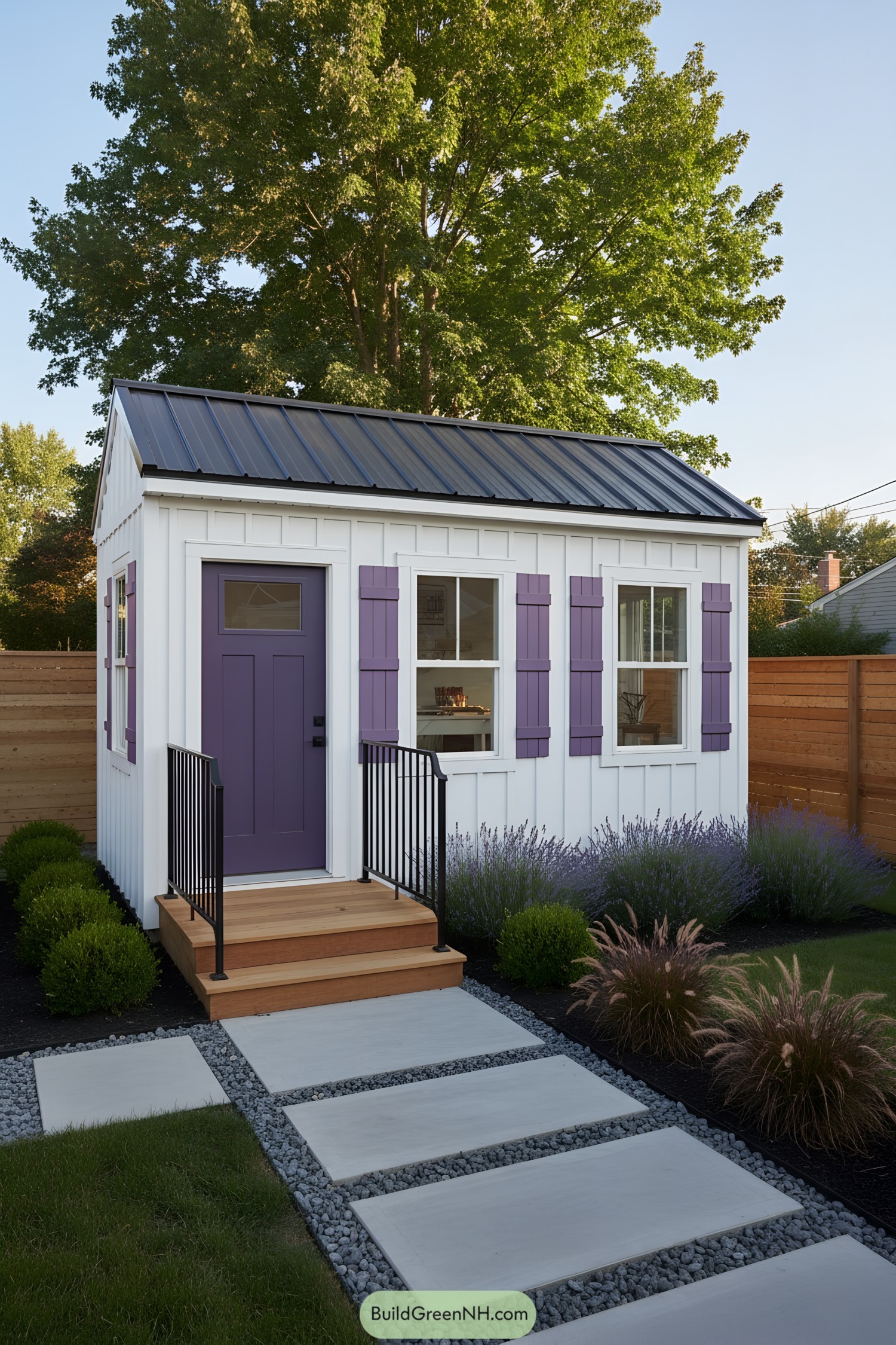 Small white shed with purple door and shutters, black metal roof, and tidy garden path