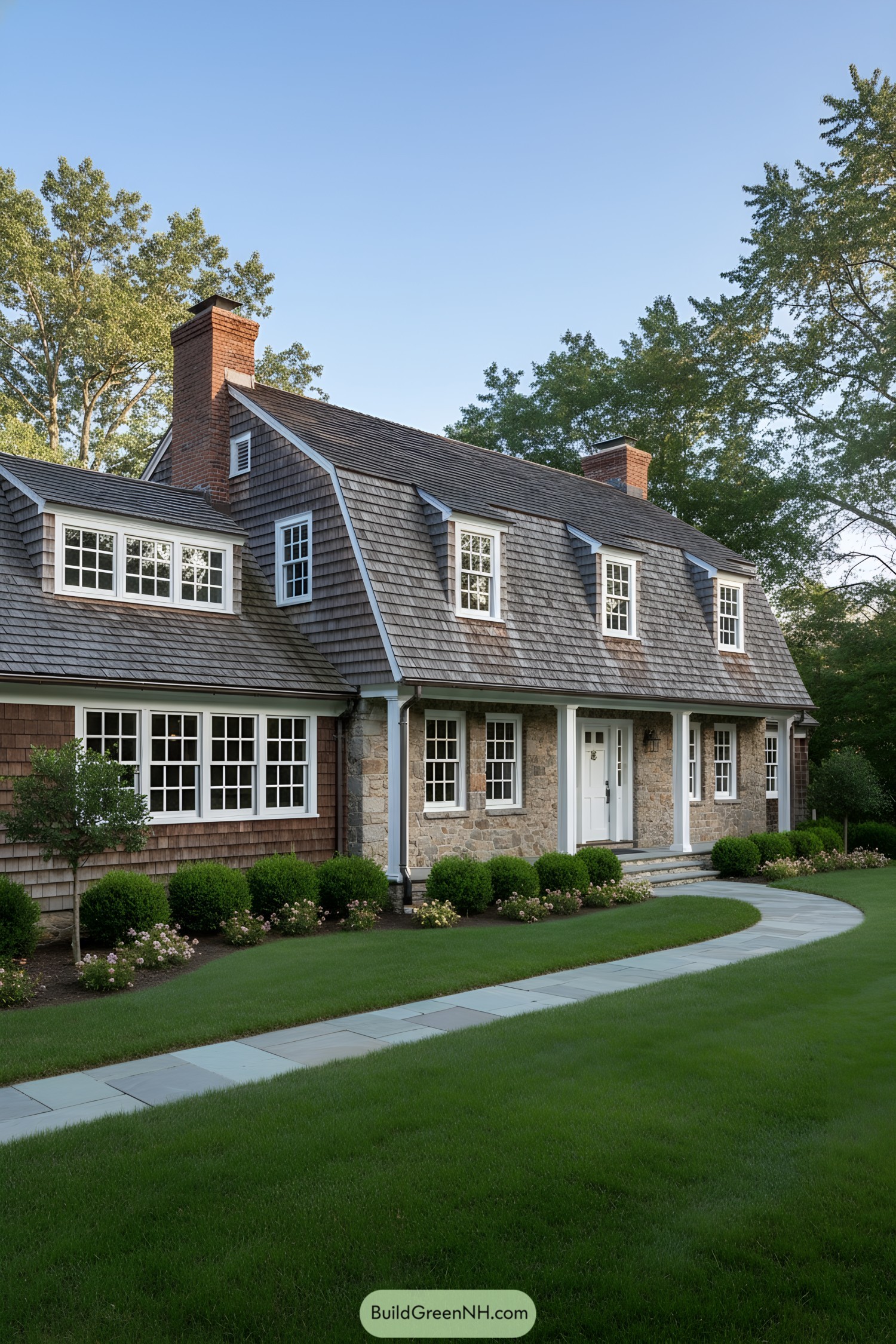 Gambrel-roof colonial with stone facade and cedar shingles, white windows, and brick chimneys