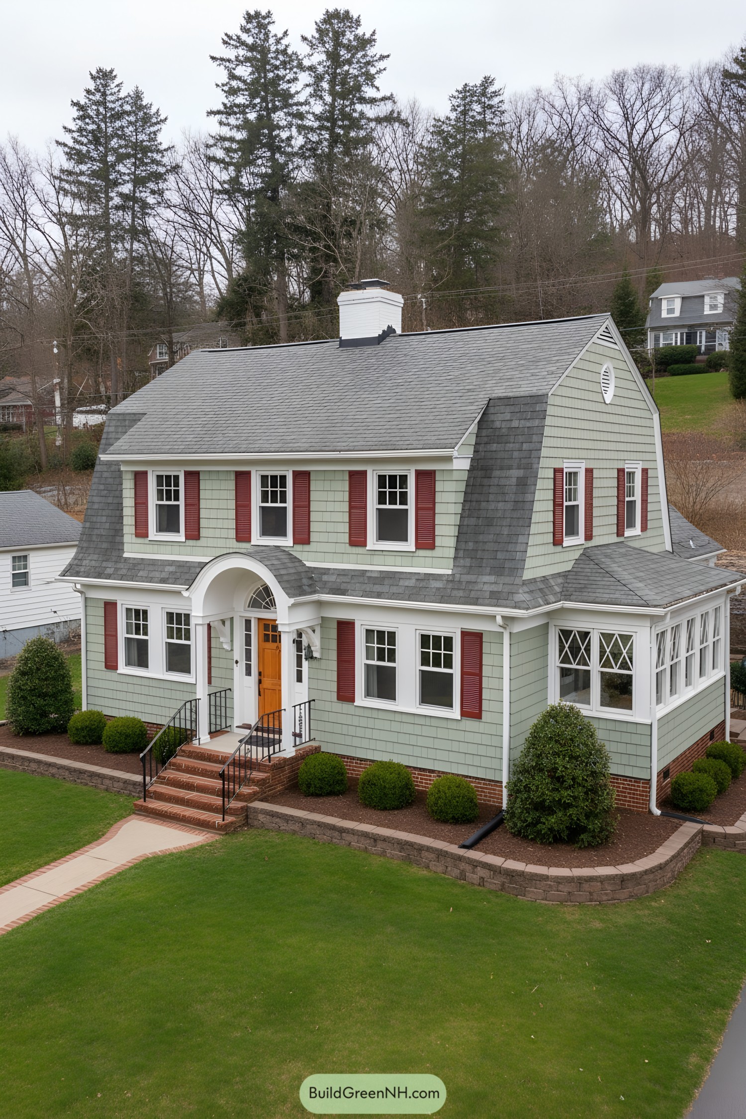 Dutch Colonial home with mint shingles, red shutters, and arched entry