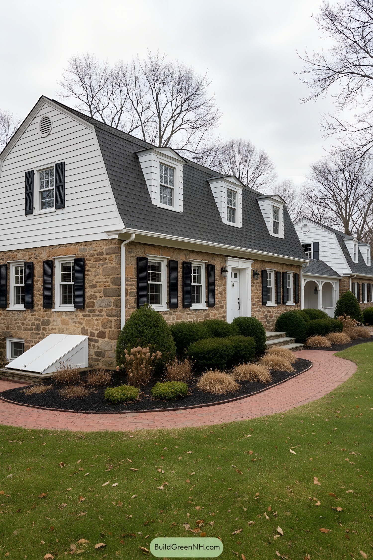 Dutch Colonial home with stone first level, white clapboard gambrel, black shutters, and dormers along a gray shingle roof