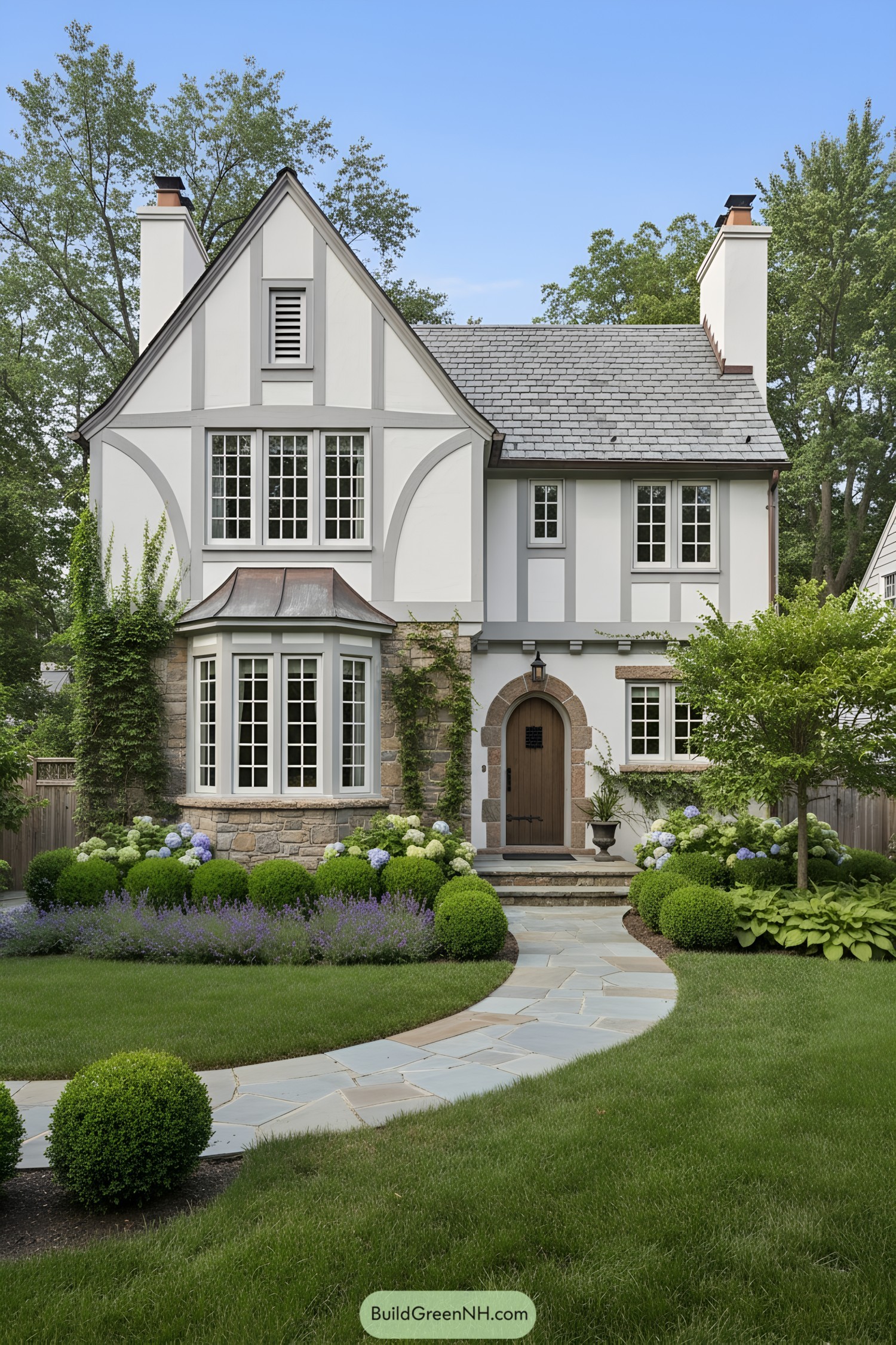 White-and-gray Tudor with copper bay, arched oak door, and manicured garden path