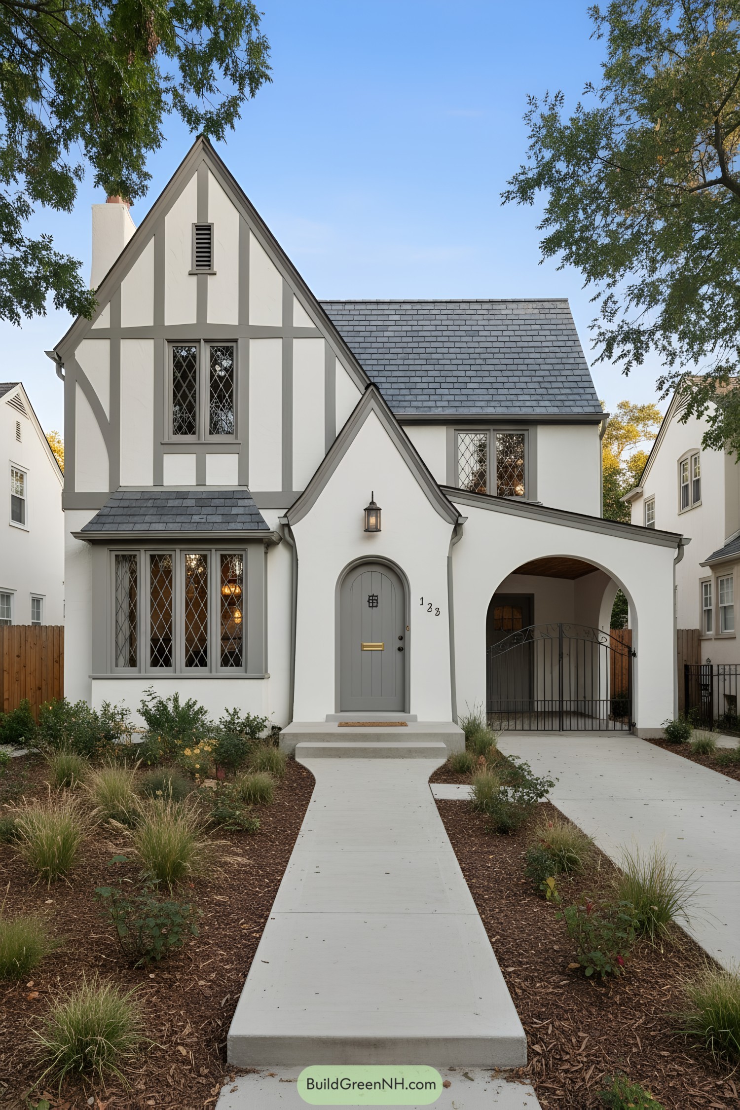 White stucco Tudor house with gray half-timbering, steep slate roof, and arched entry
