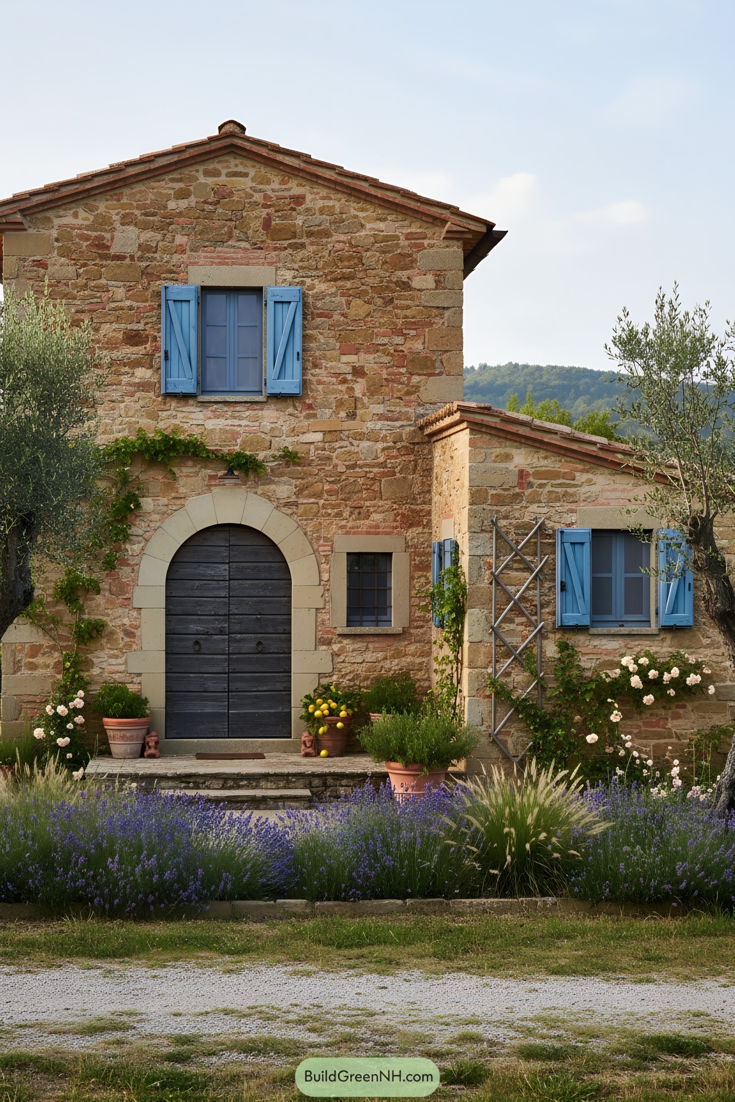 Rustic stone cottage with blue shutters, arched wood door, and lavender-lined entry