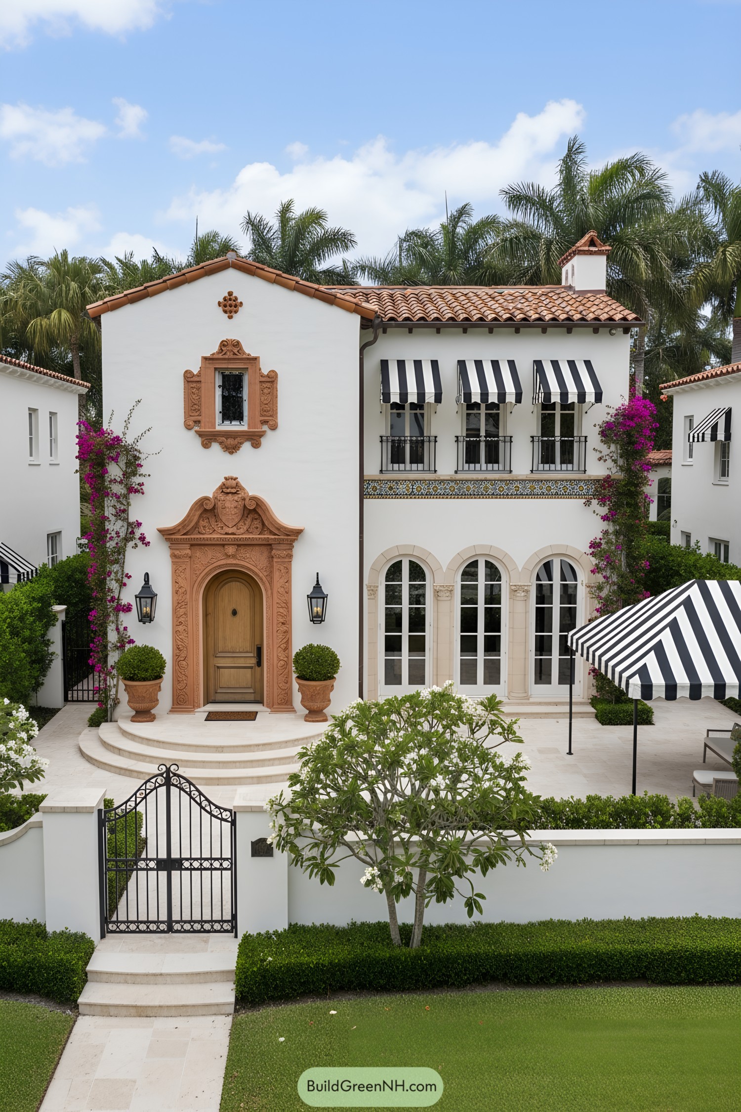 White stucco villa with terracotta trim, striped awnings, arched doors, and lush courtyard