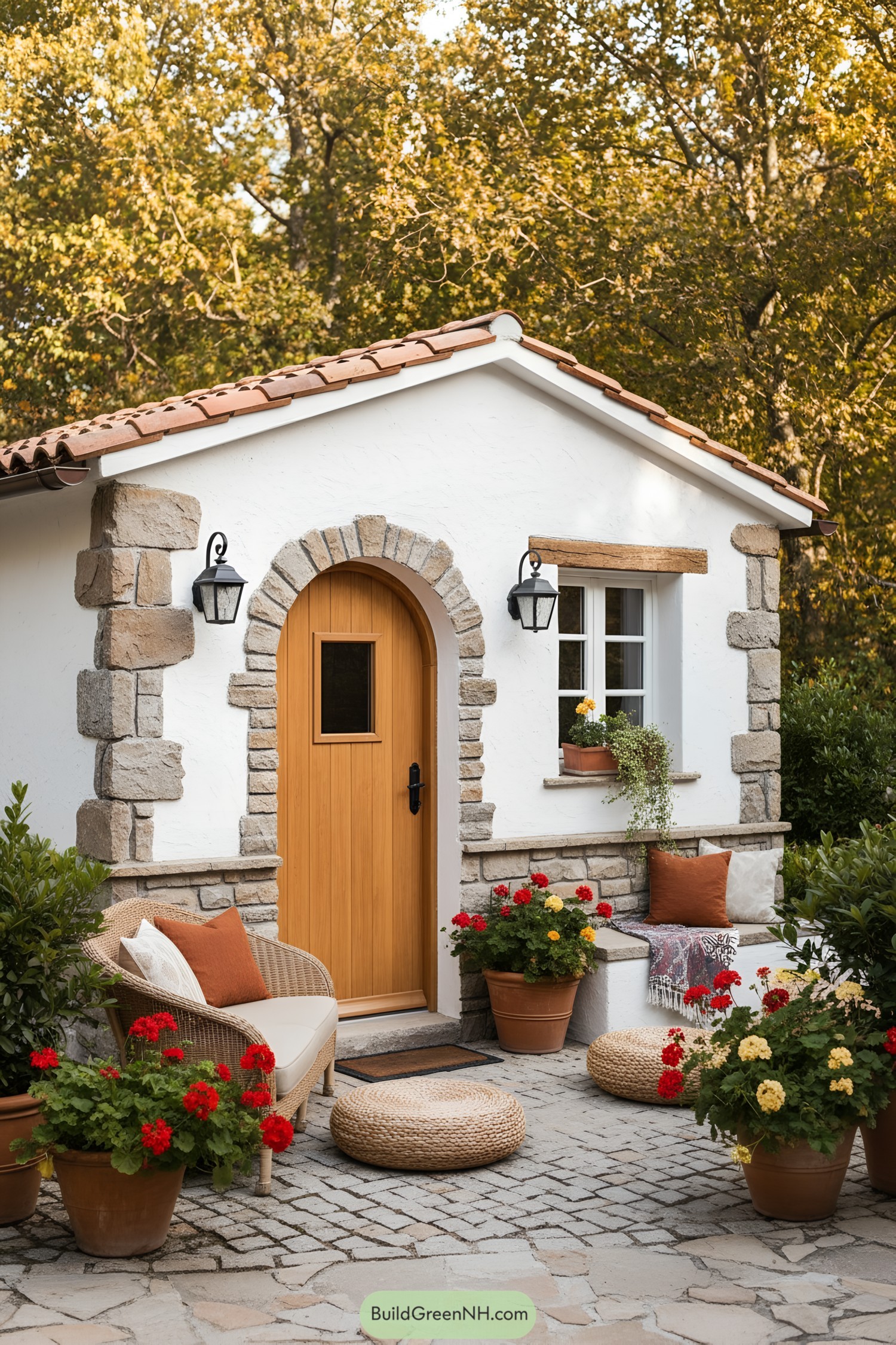 Small white stucco cottage with arched wood door, stone trim, terra-cotta roof, and cozy garden patio
