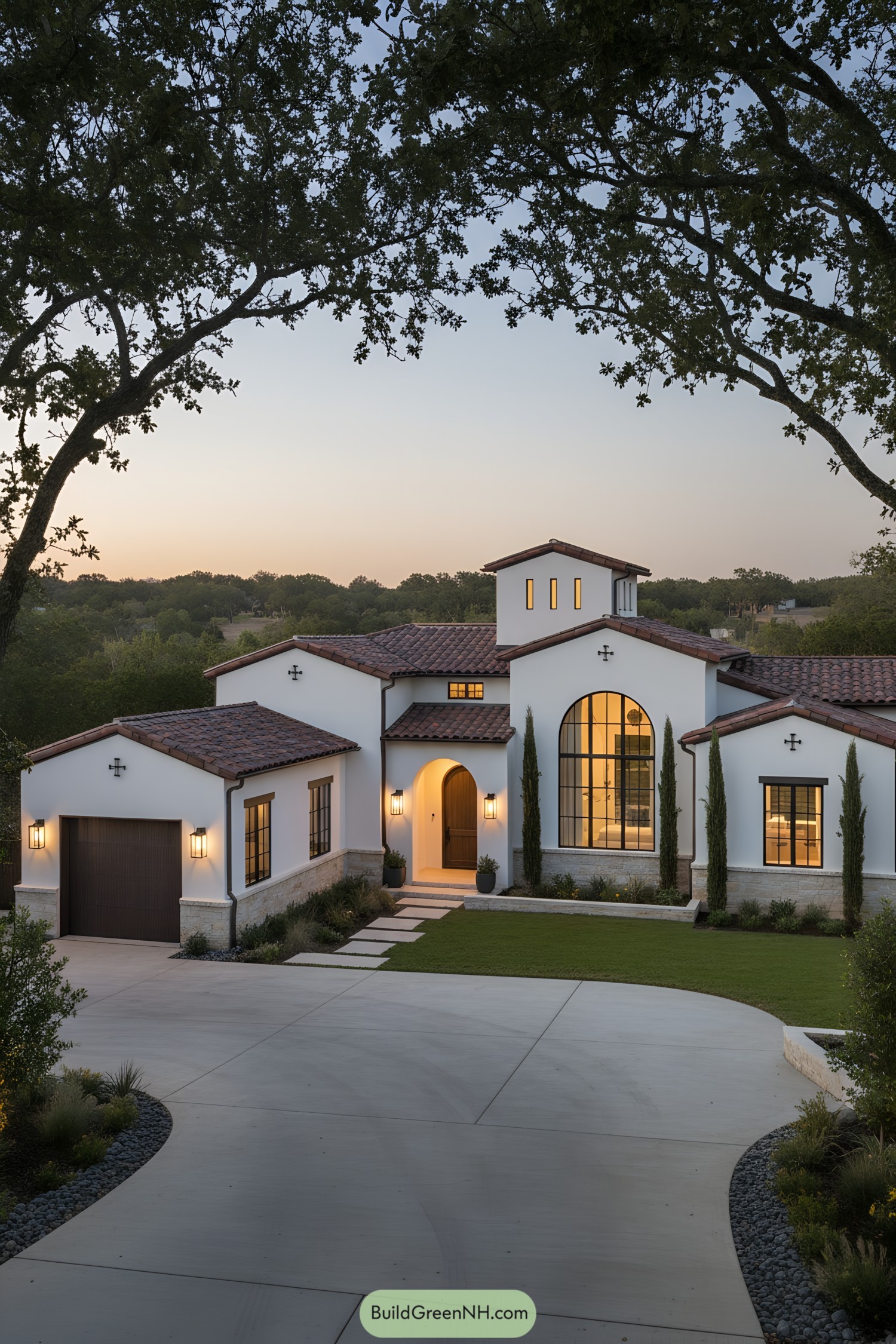 White stucco farmhouse with red tile roofs, arched entry, tower, and cypress-lined facade at dusk