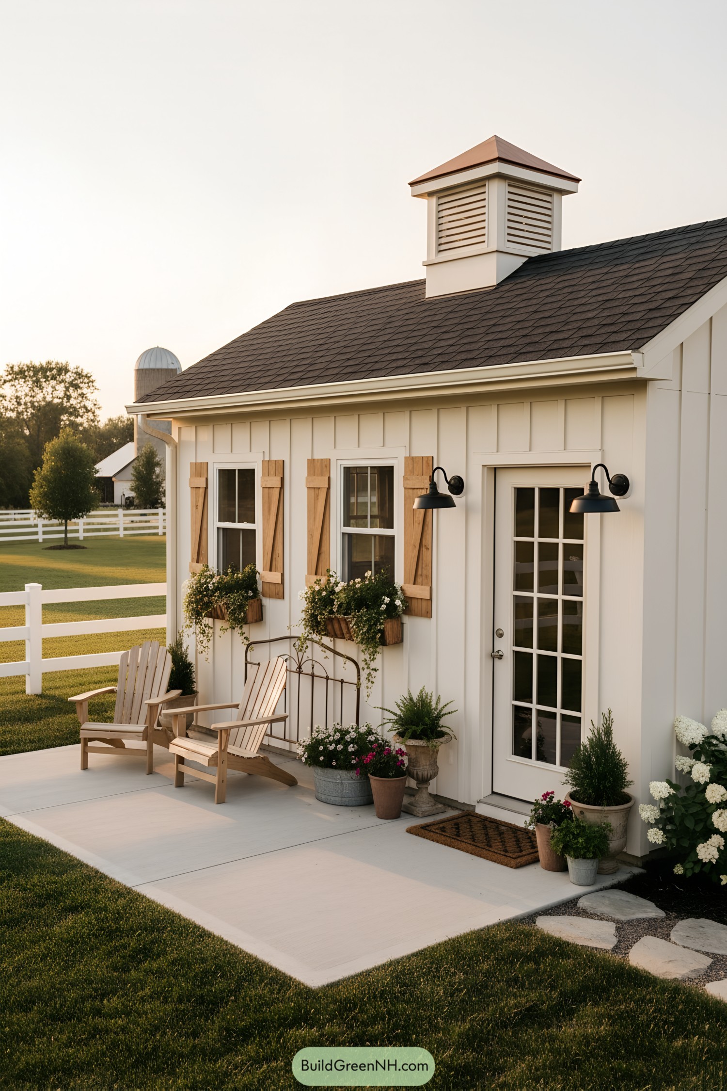 Cream shed with cupola, wood shutters, and flower boxes by a small patio