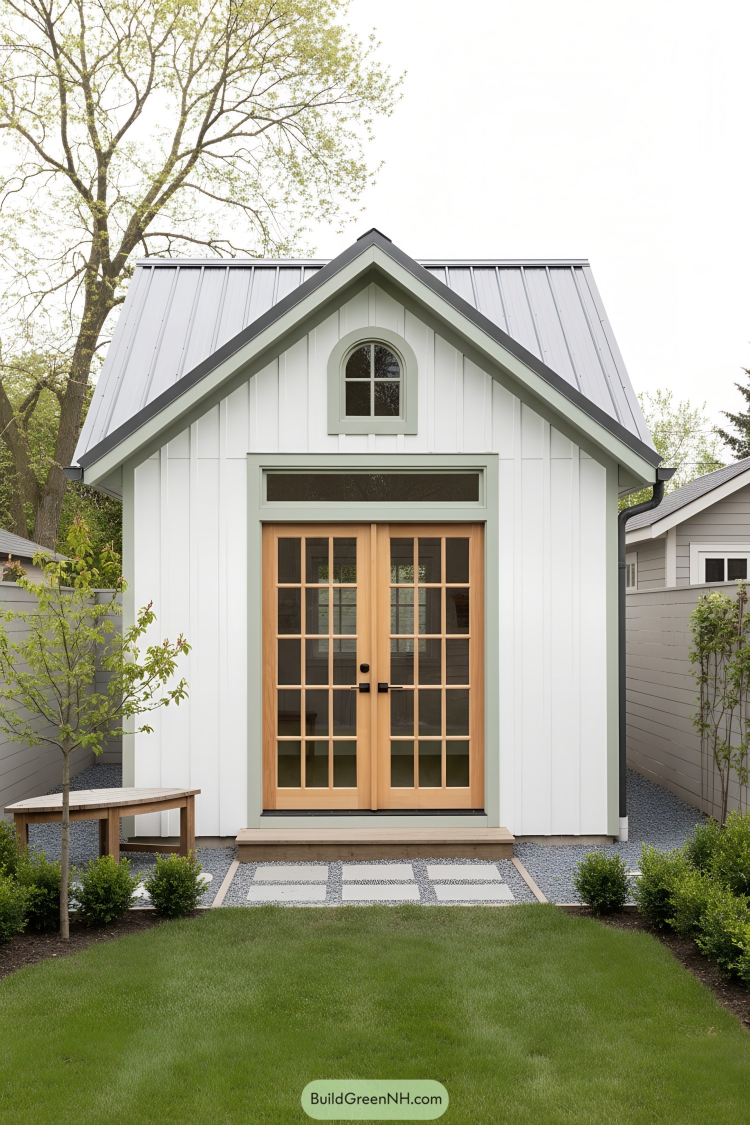 Small white garden studio with mint trim and arched window over wood French doors