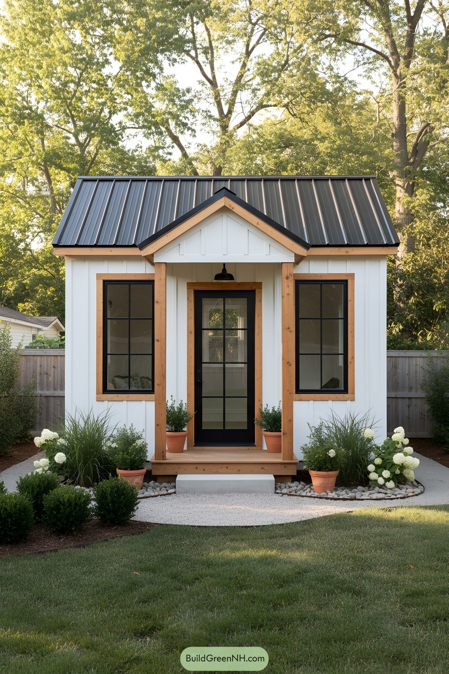 Small white shed with black metal roof, natural wood trim, and black French door flanked by windows
