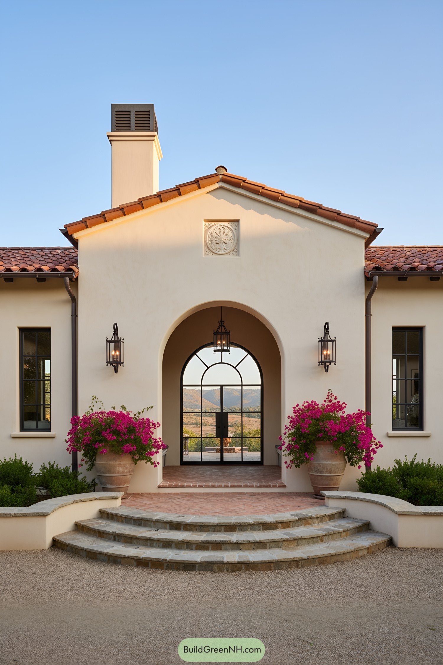 Spanish Colonial entry with arched steel door, terracotta roof, and bougainvillea planters