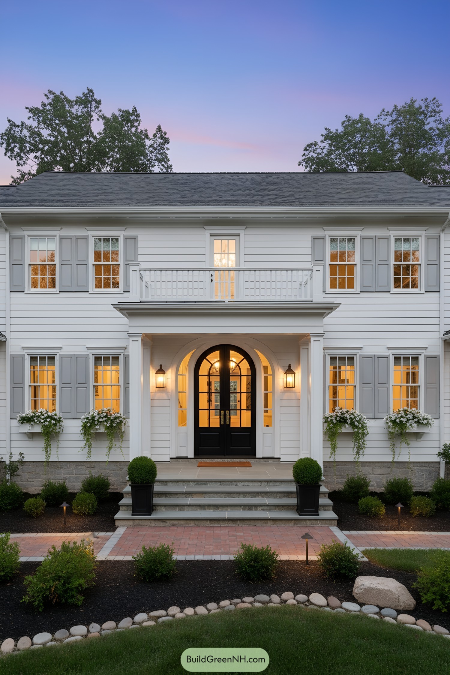 White clapboard colonial with gray shutters, arched double door, and small balcony over the porch